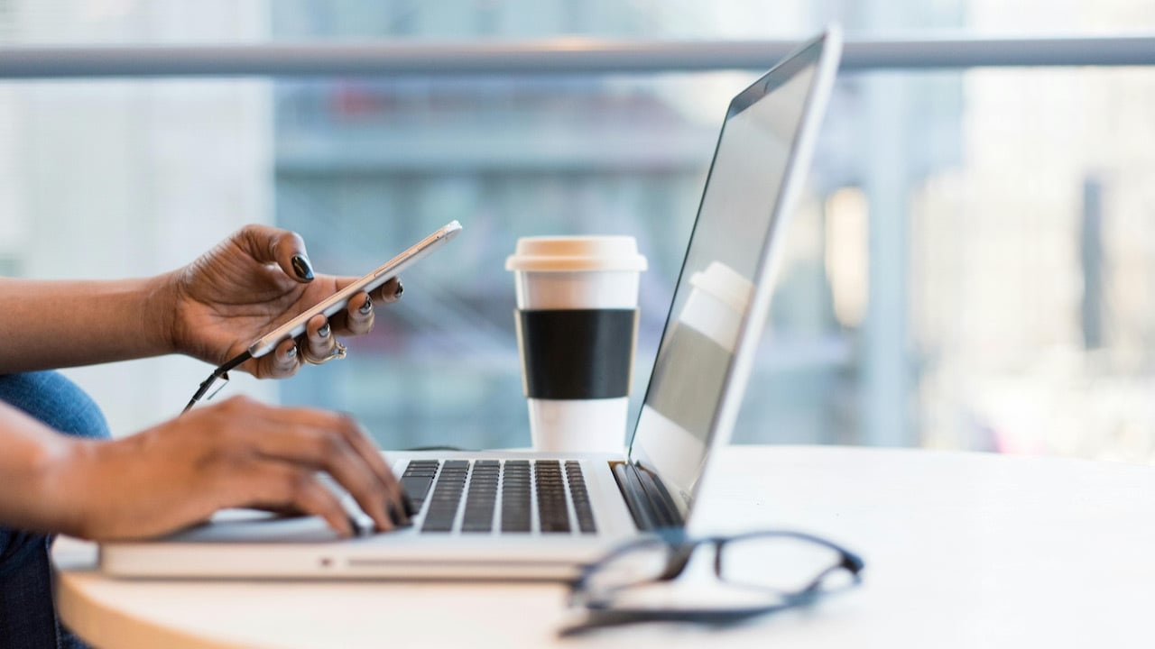 woman holding phone and looking at computer