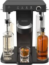 black cocktail machine with bottles of alcohol on both sides. In the middle is a shot glass filled with brown liquor