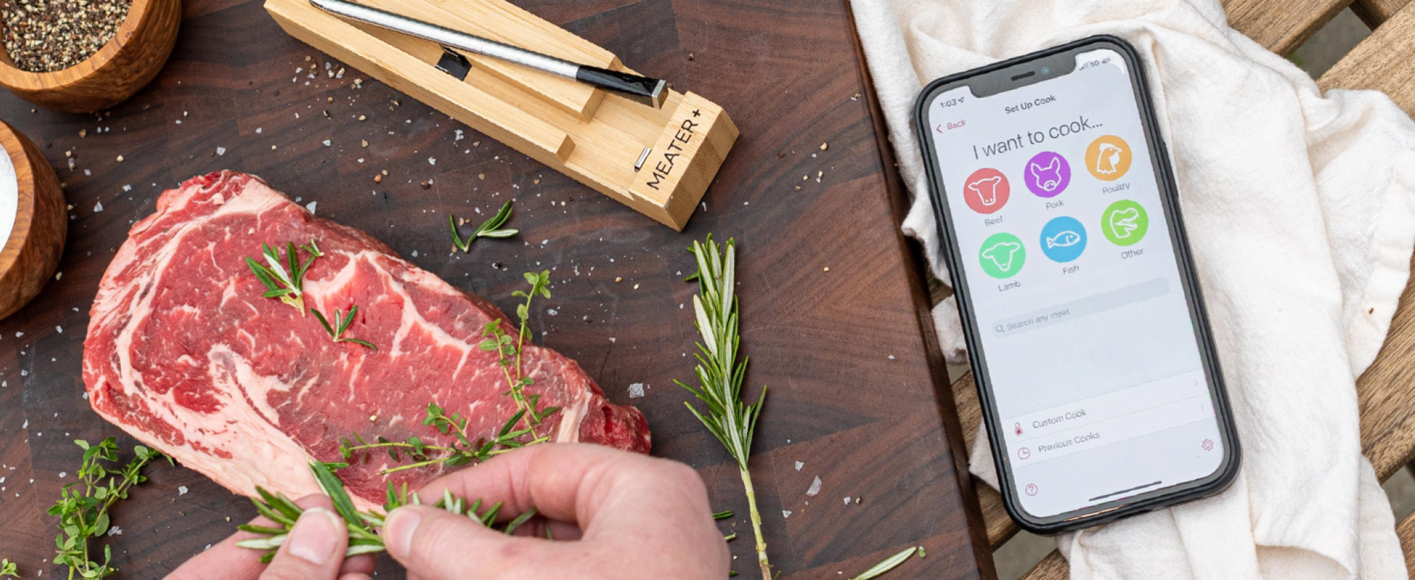 hands seasoning meat next to meater app