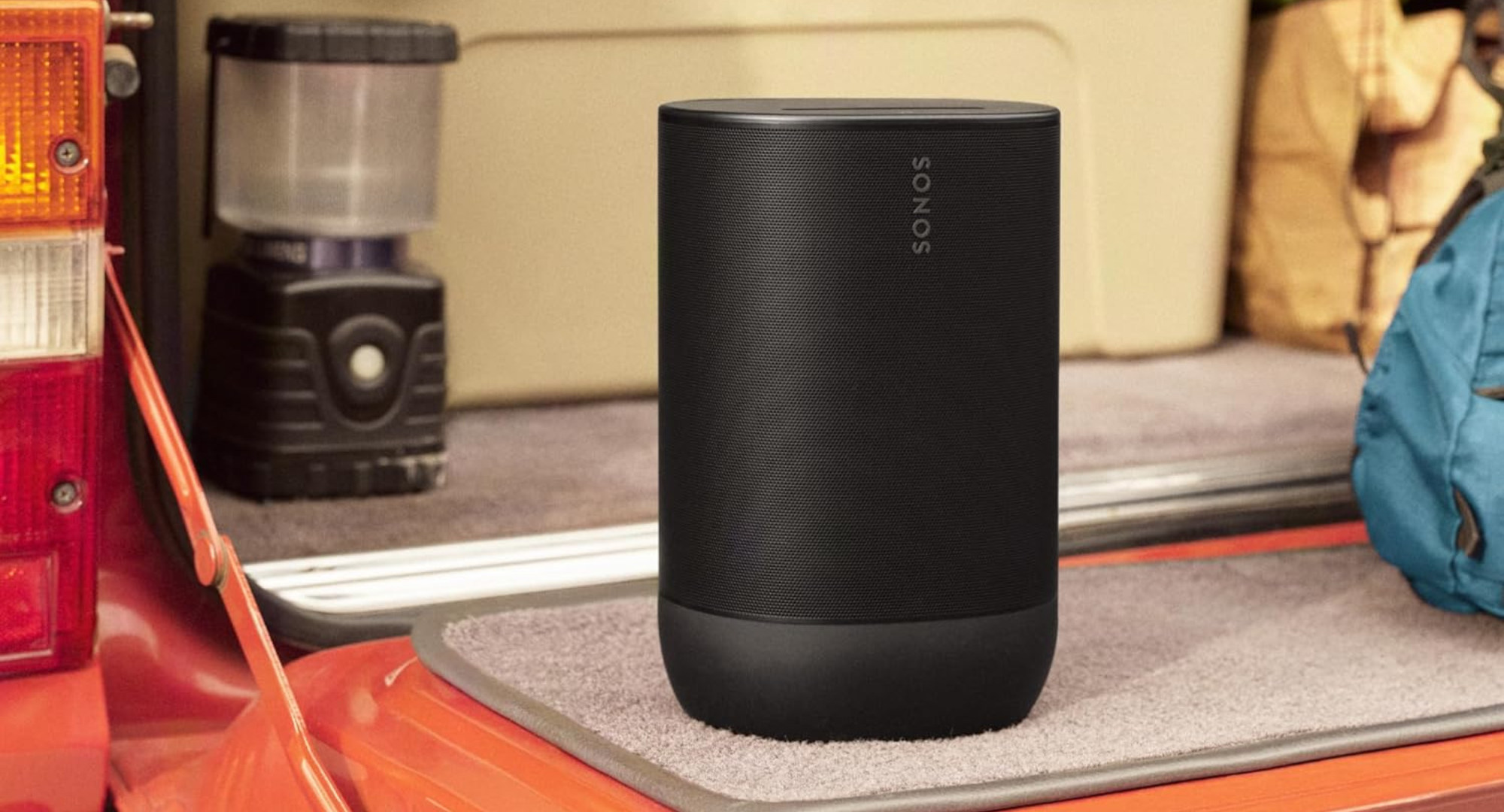 A black Sonos Move 2 portable speaker sits on the open tailgate of an SUV, with camping gear in the background.
