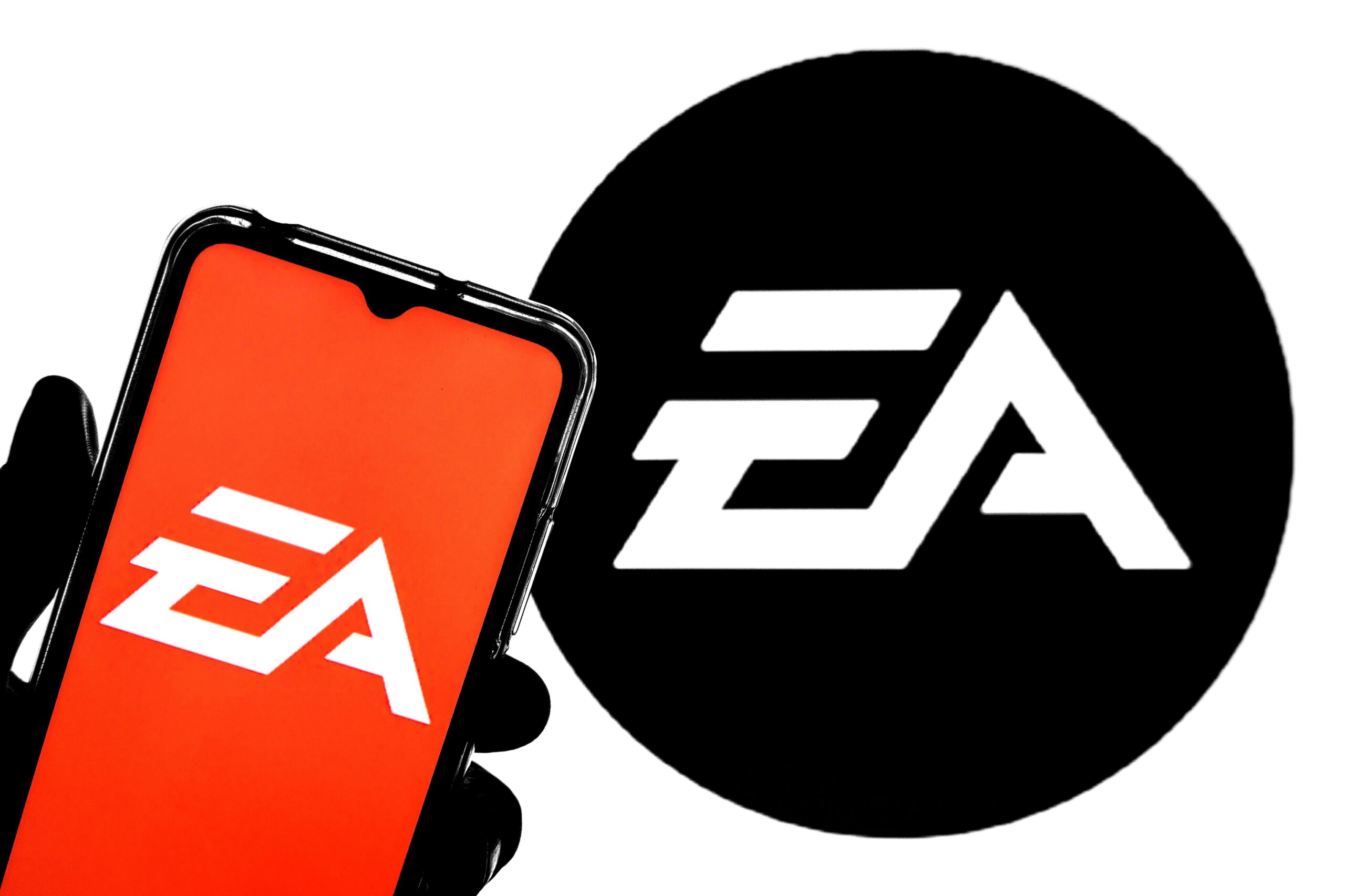 An iPhone displaying an orange EA logo is held in front of a larger black EA logo.