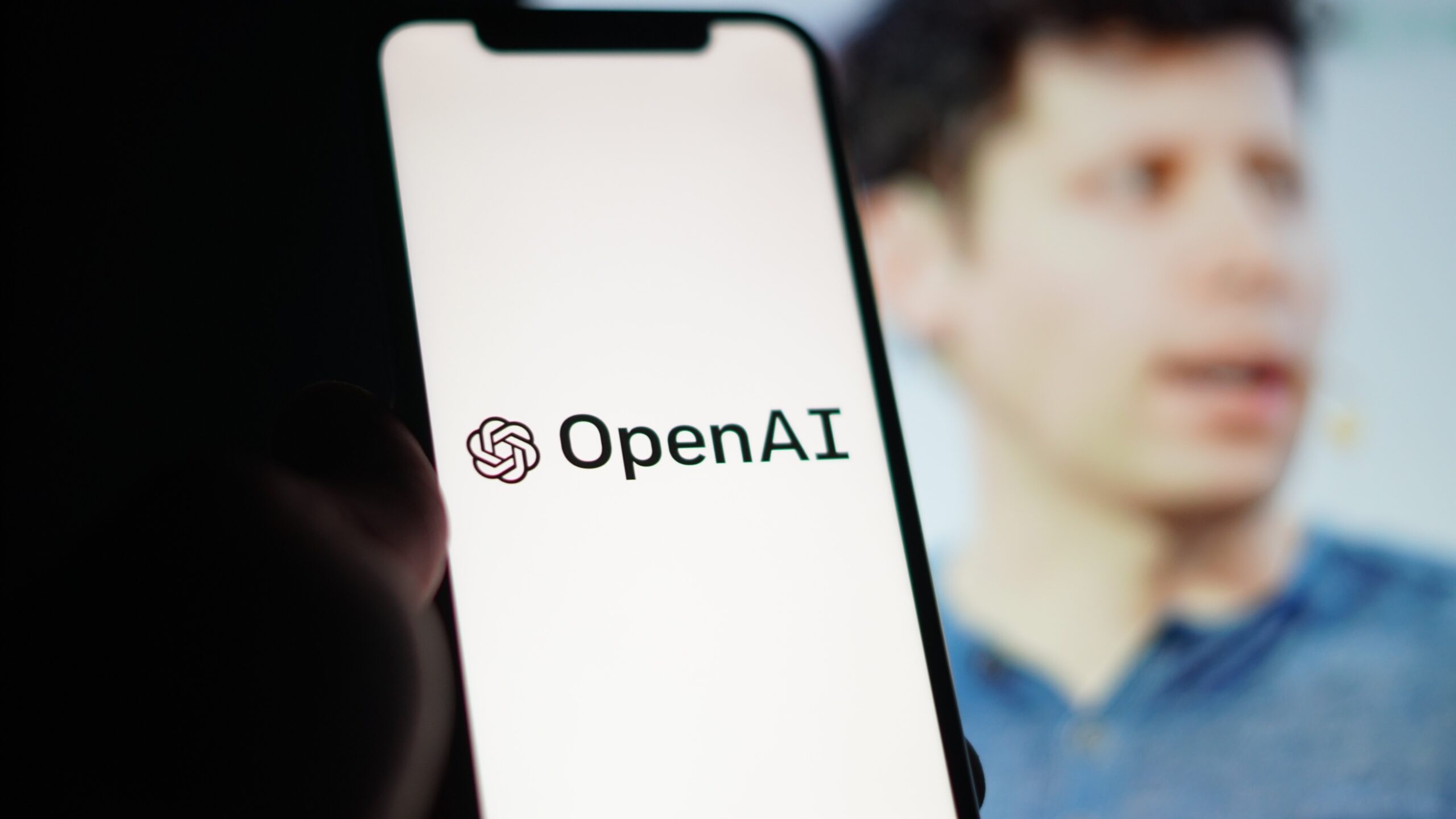 openai logo on a smartphone in front of an image of ceo sam altman