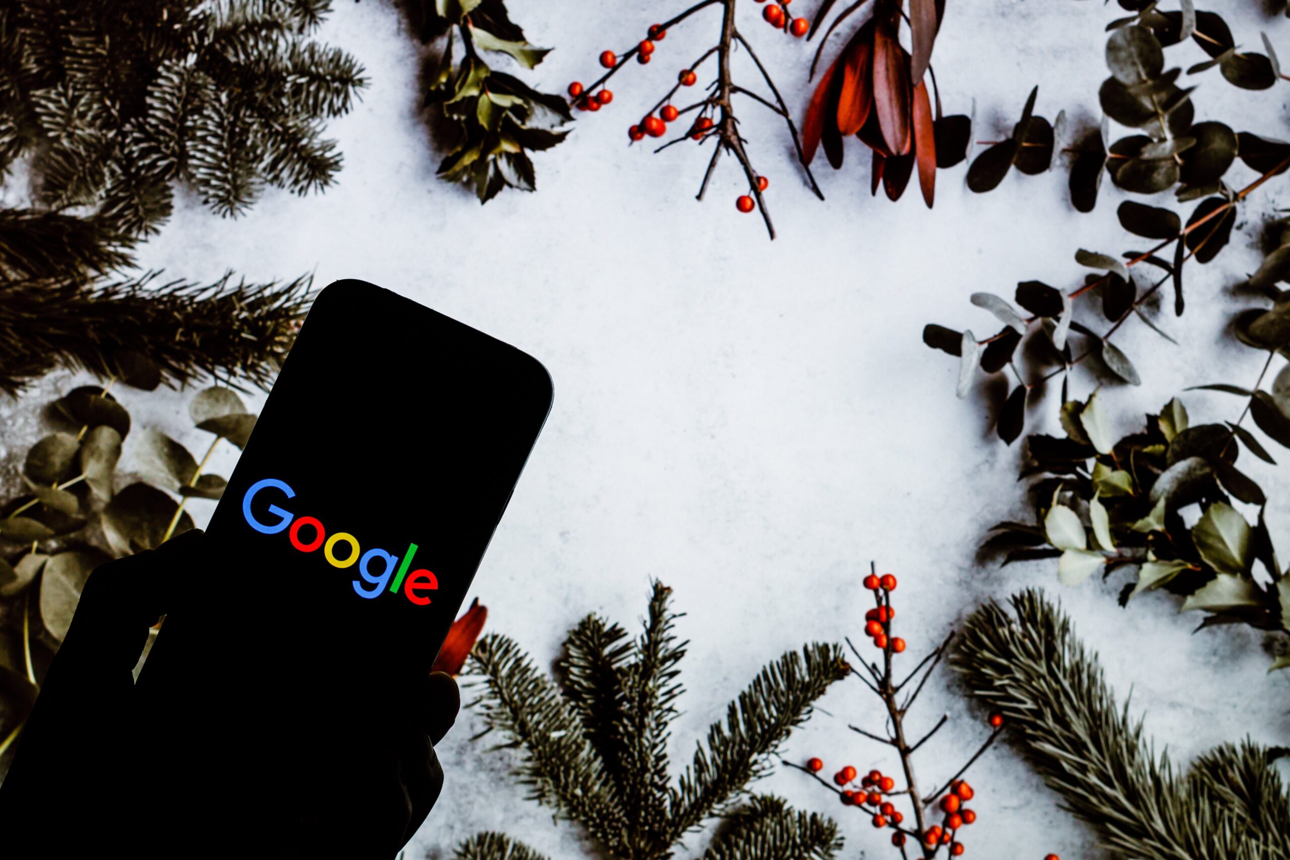 a phone displaying the Google logo surrounded by boughs of holly and such