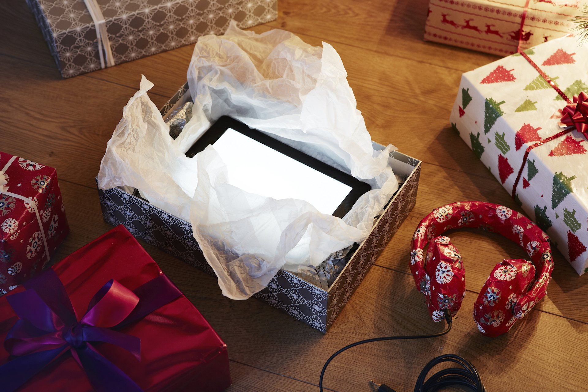Wrapped and unwrapped presents on the floor, including a tablet and headphones.