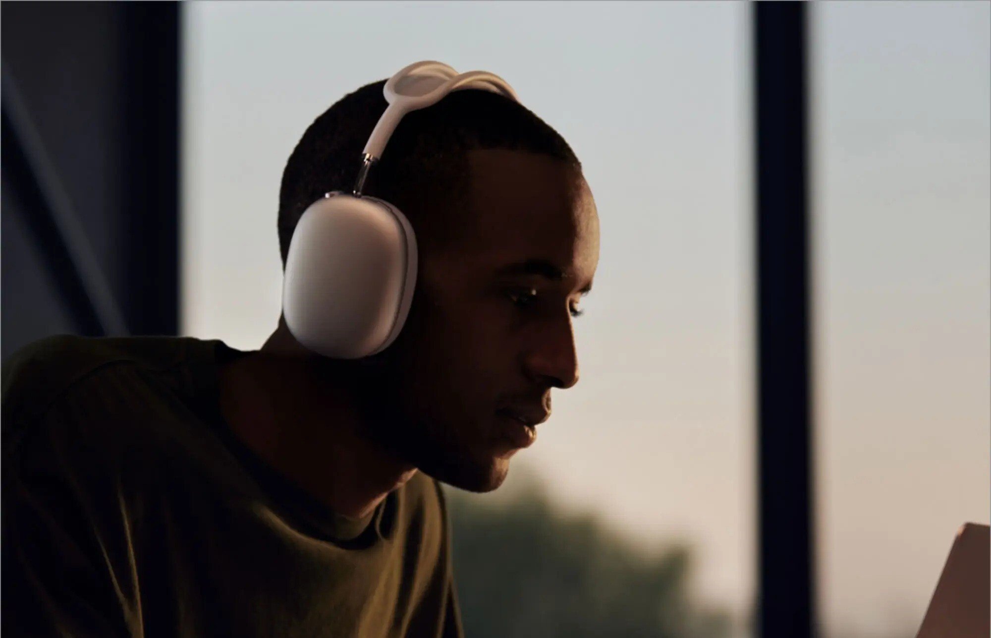 a person wears the apple airpods max headphones while looking at a computer screen in a dimly lit room