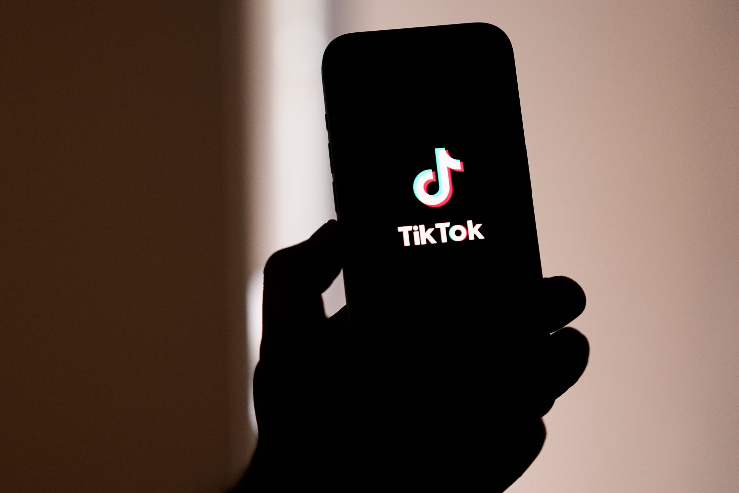 A backlit hand holds up a phone displaying the TikTok logo.