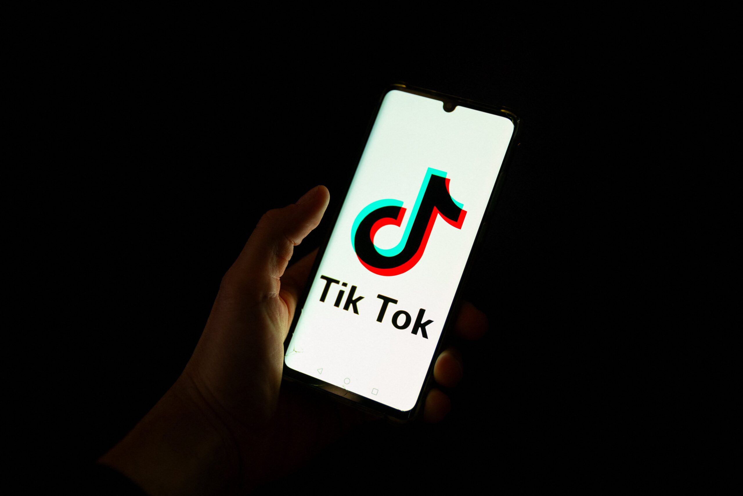 This photograph taken on April 19, 2024 shows a man holding a smartphone displaying the logo of Chinese social media platform Tiktok in an office in Paris