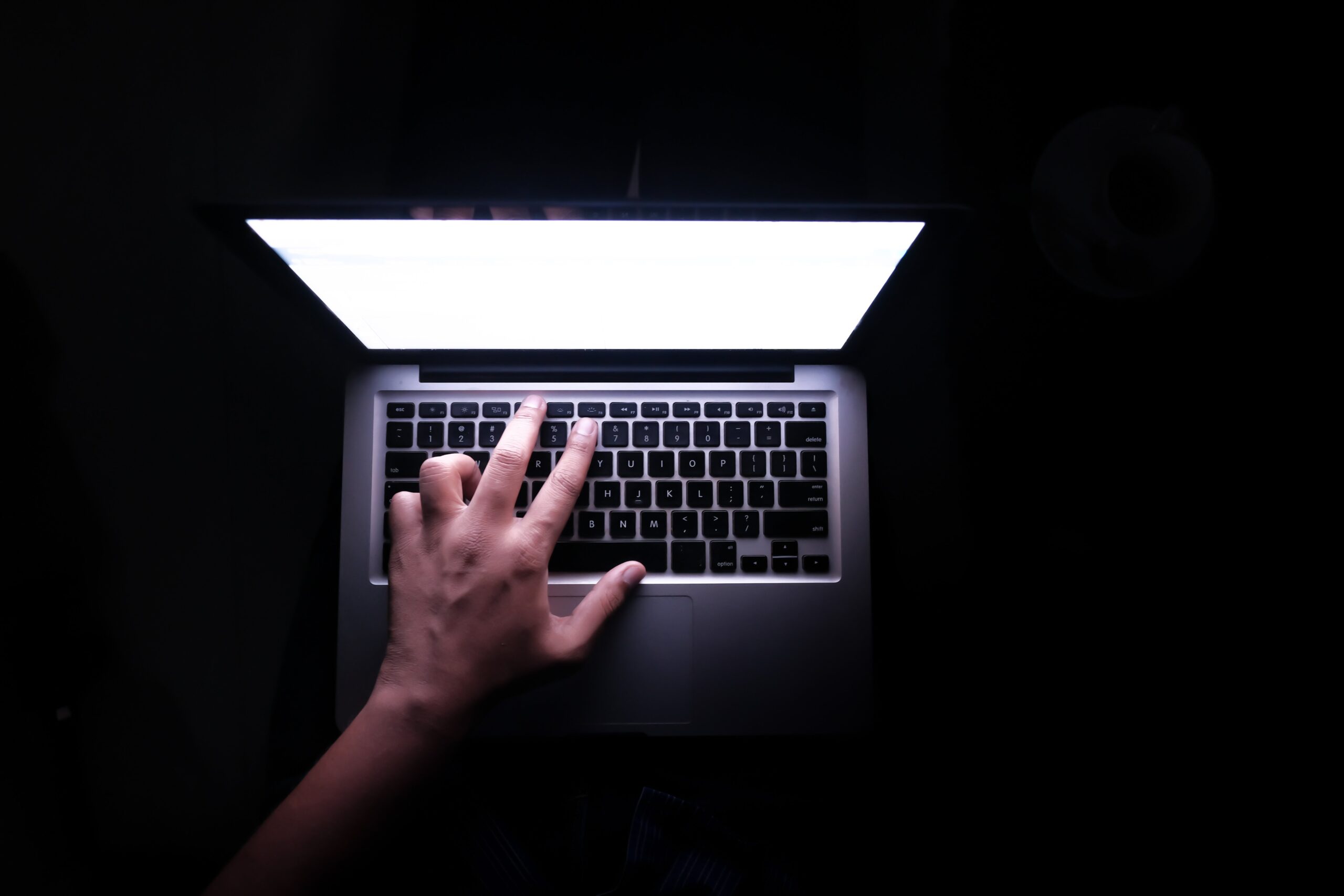 A hand hovers ominously over a keyboard against a dark background. 