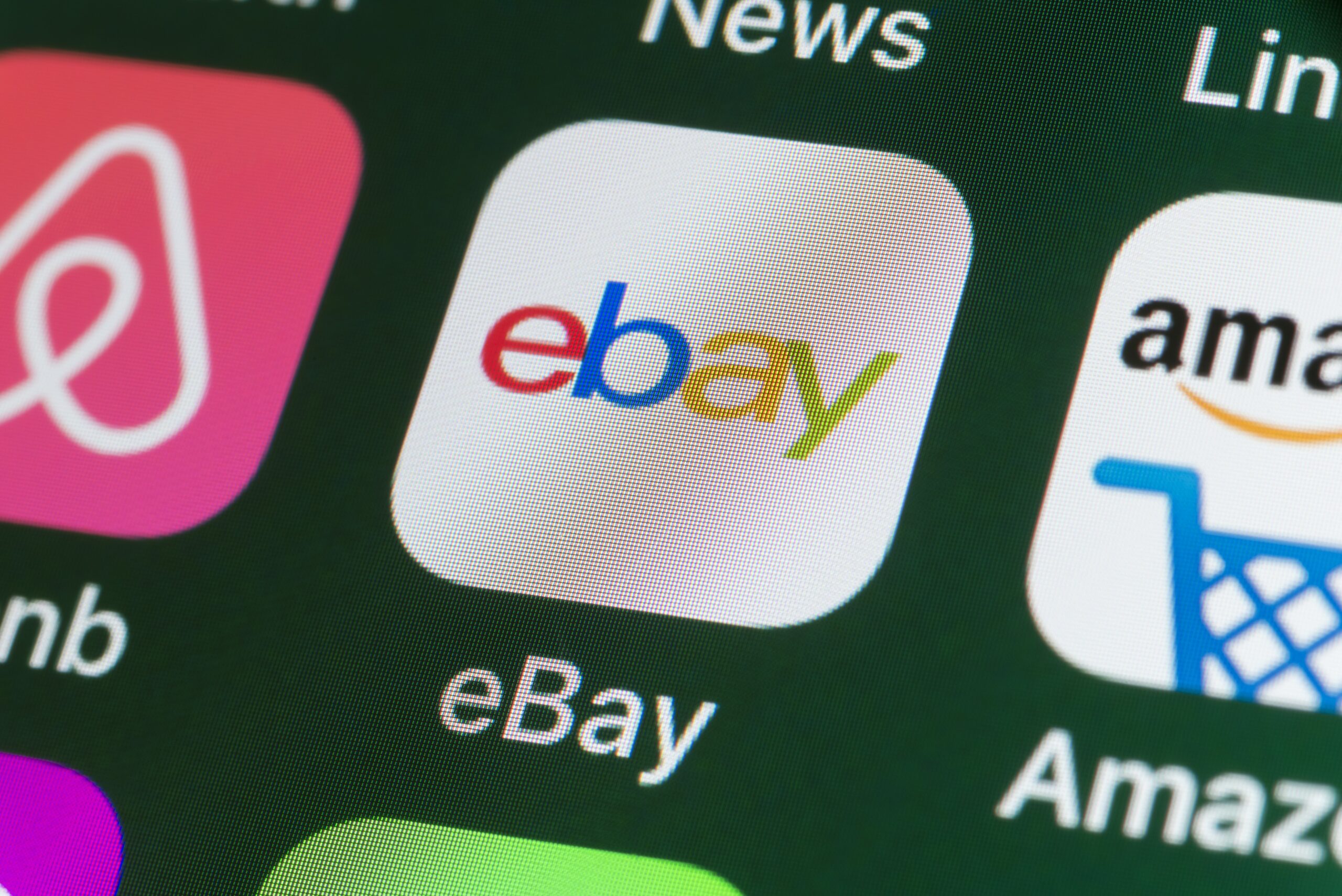 The buttons of the online shopping app ebay, surrounded by Airbnb, Amazon, News and other apps on the screen of an iPhone.