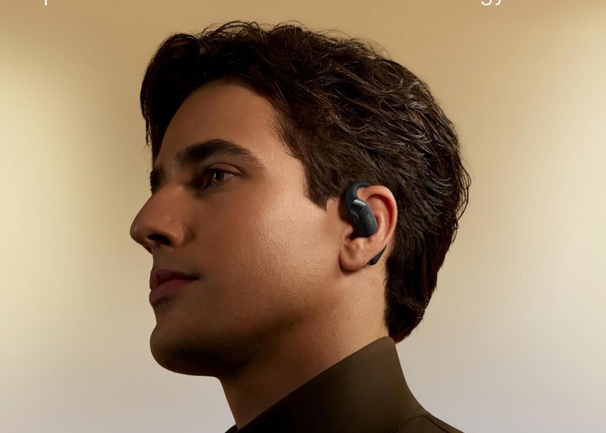 a person wearing the shokz openfit 2 earbuds gives a profile look against a cream-colored background while wearing a brown turtleneck 