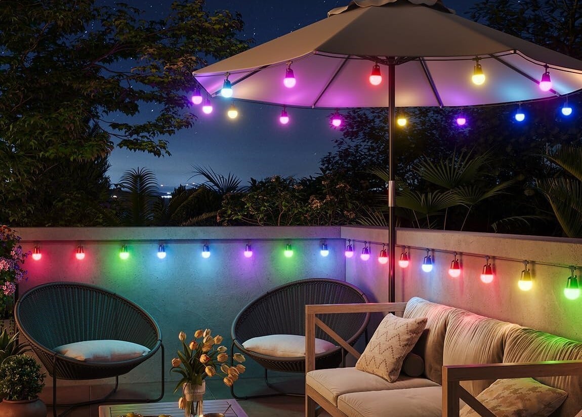 the govee smart outdoor string lights 2 on a back patio, displayed around the bottom permitter of a sun umbrella over a table and along a deck railing