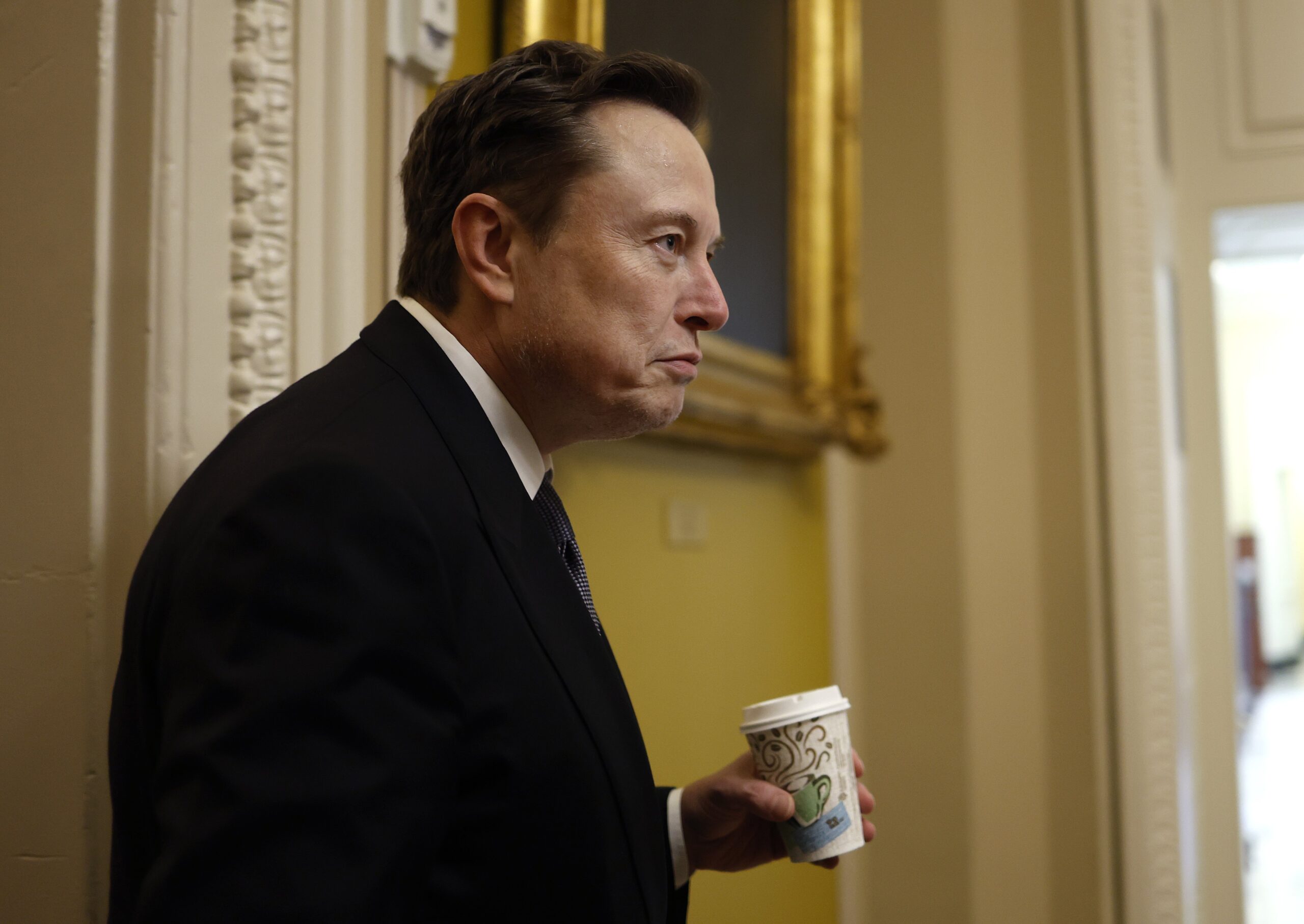 white man in black suit carrying a disposable coffee cup