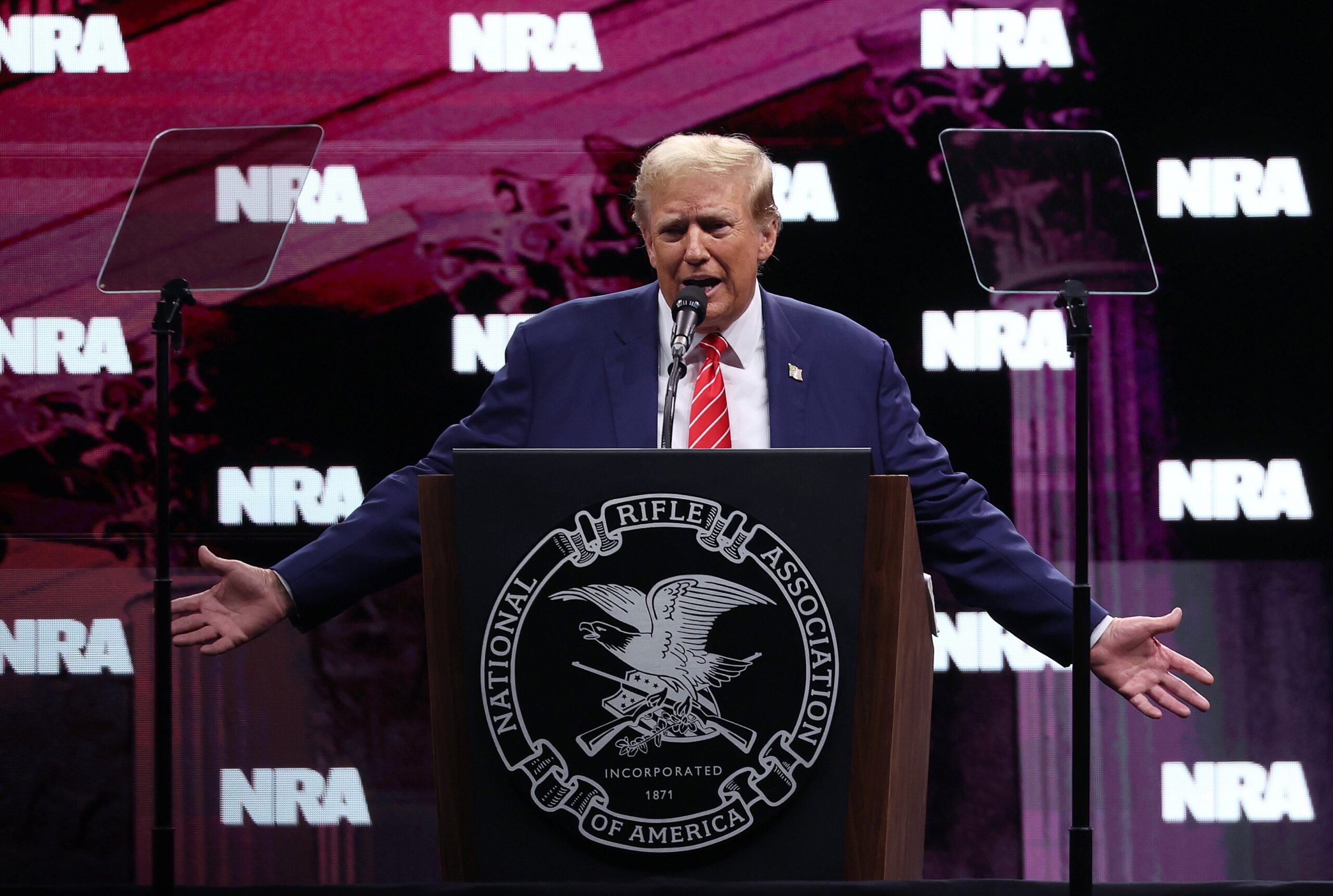 Trump stands in front of a podium on stage at the National Rifle Association (NRA) annual meeting. 