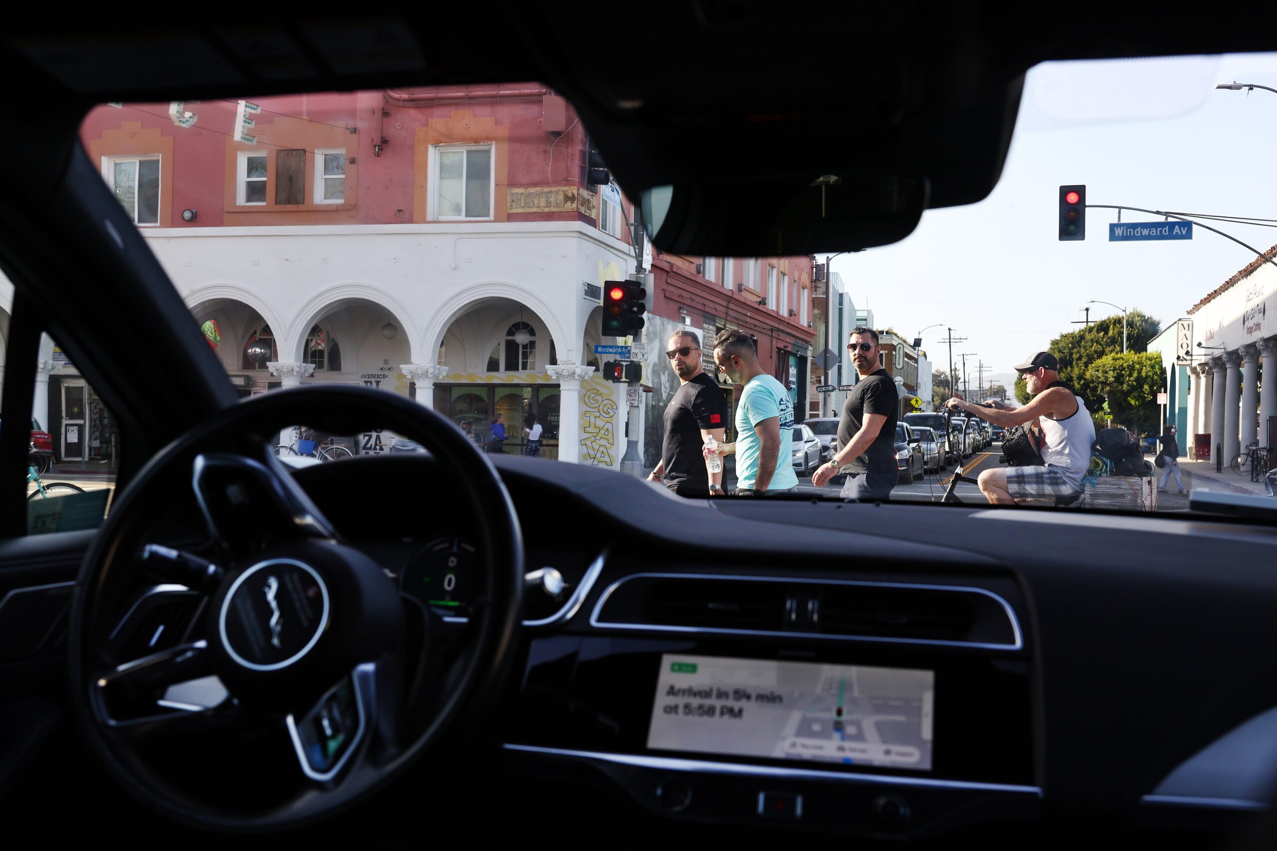 Pedestrians look toward a Waymo autonomous self-driving Jaguar taxi stopped at a red light near Venice Beach