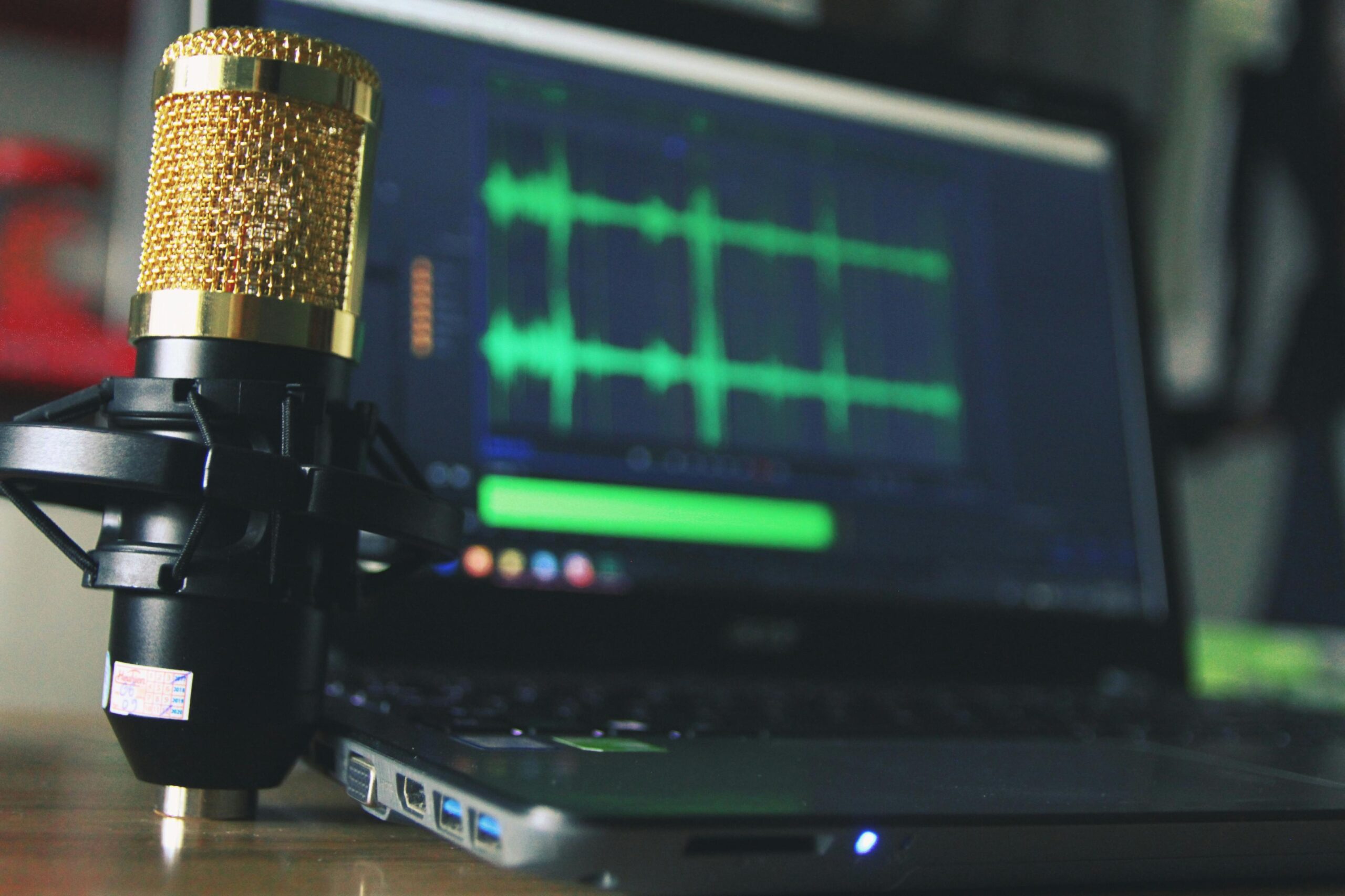 a condenser microphone next to a laptop with audio editing software