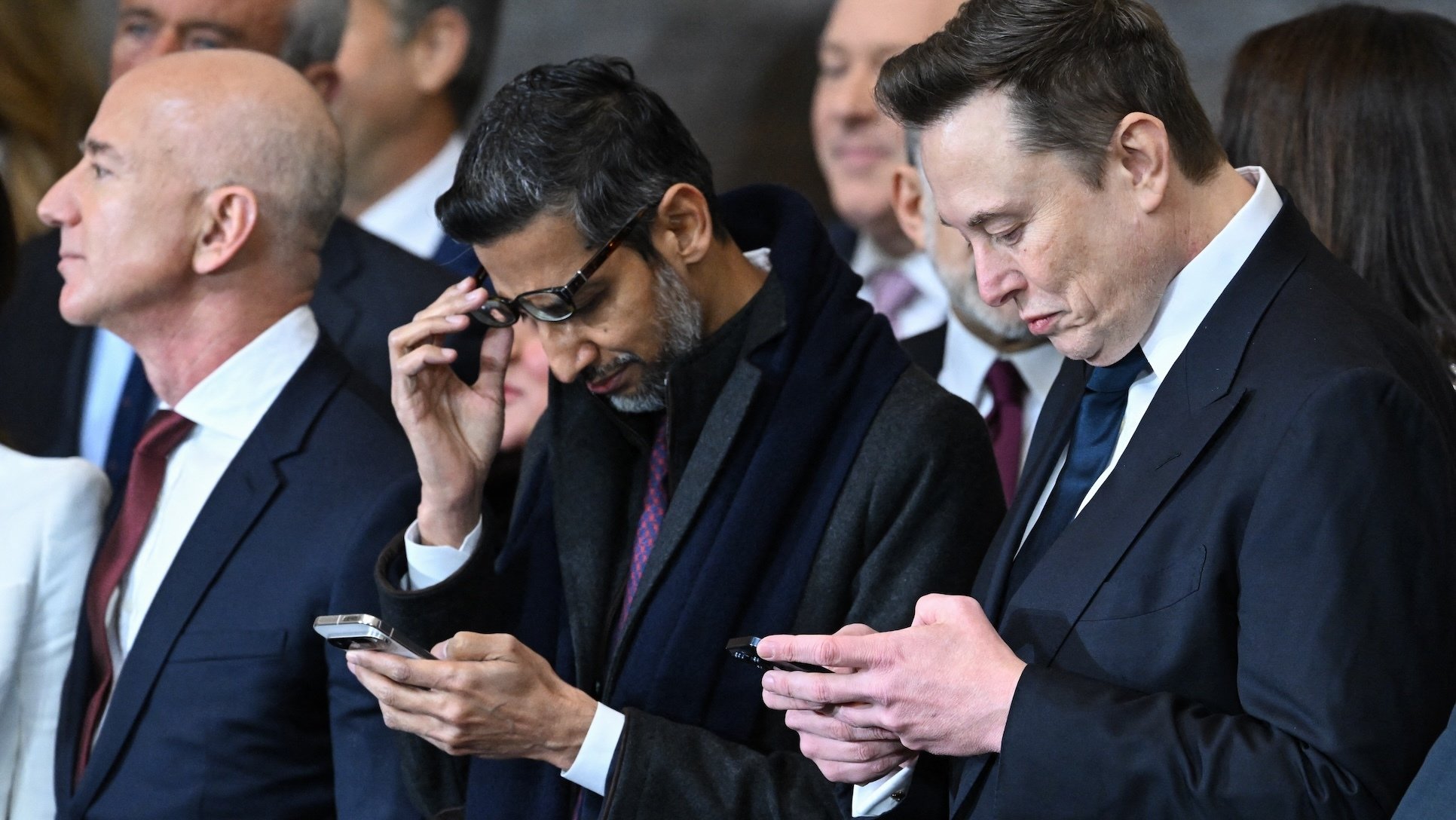 Google CEO Sundar Pichai and Tesla CEO Elon Musk look at their phones while Amazon's Jeff Bezos looks away.