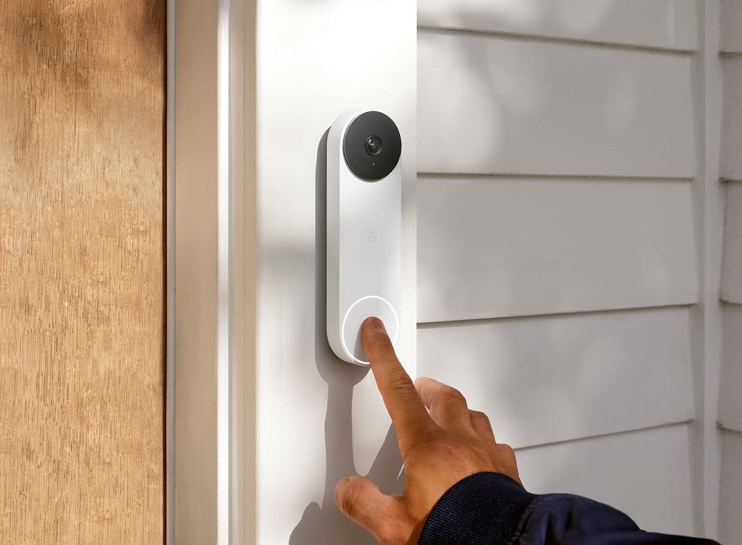 an index finger rings the google nest doorbell that's attached to a house next to the front door