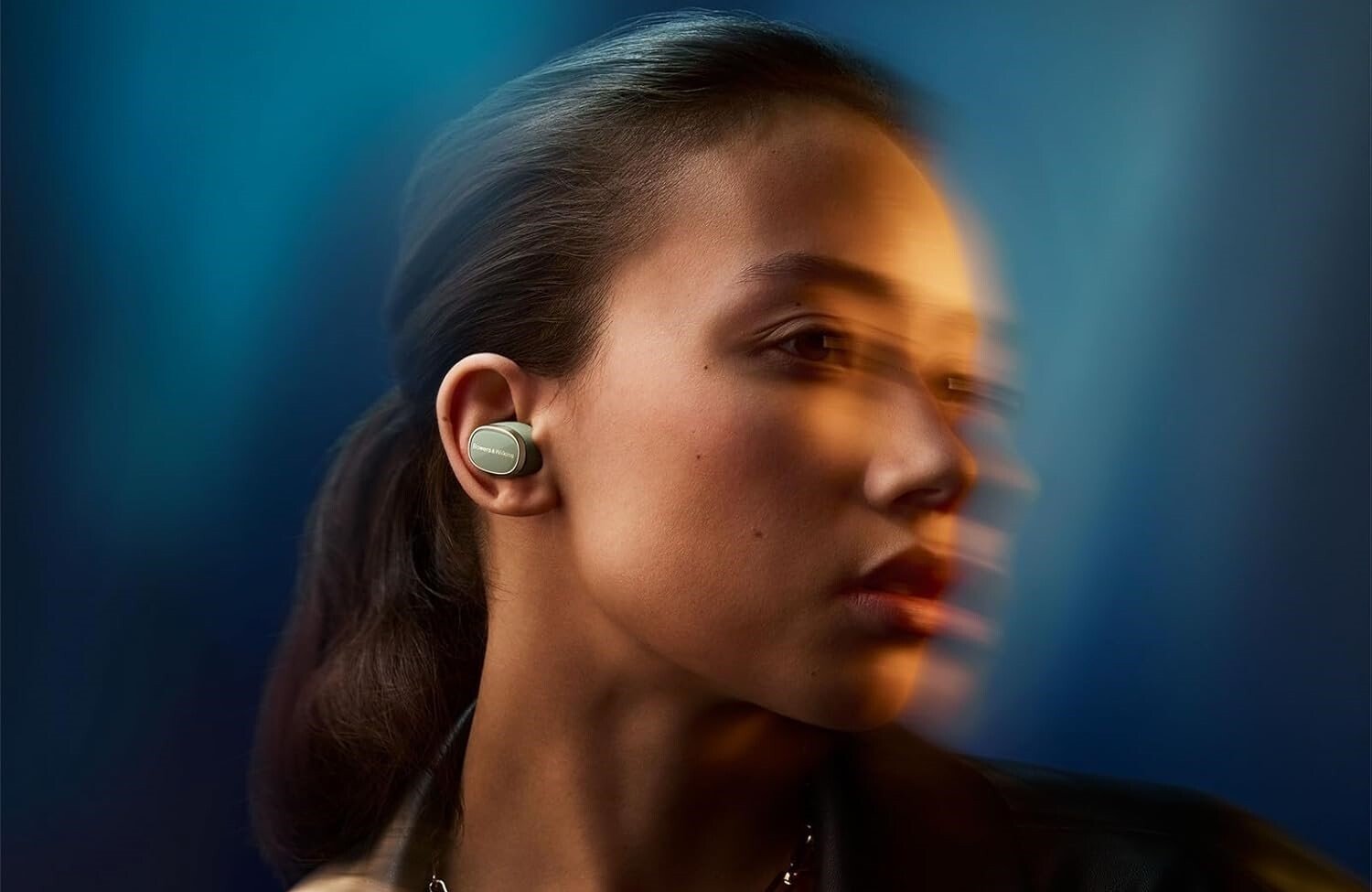 a person wearing the bowers & wilkins pi8 earbuds turns to the right in a slightly blurred motion photo with a black background