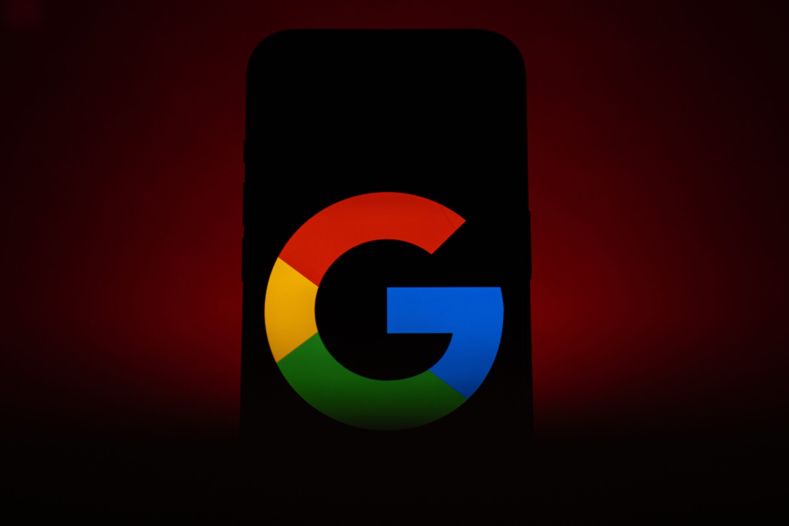 A phone in ominous red lighting displaying a Google logo.