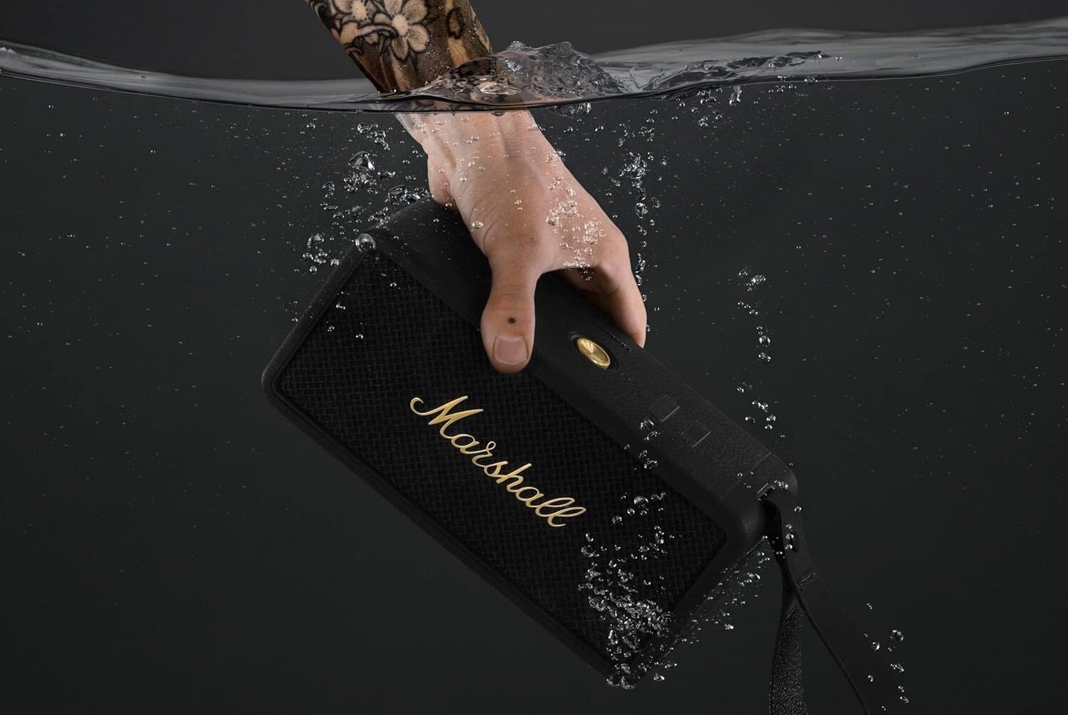 a person's left hand submerges the marshall middleton speaker into water