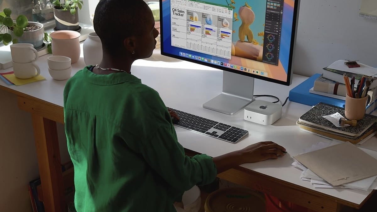 person sitting at desk with mac mini, apple magic keyboard, and apple display