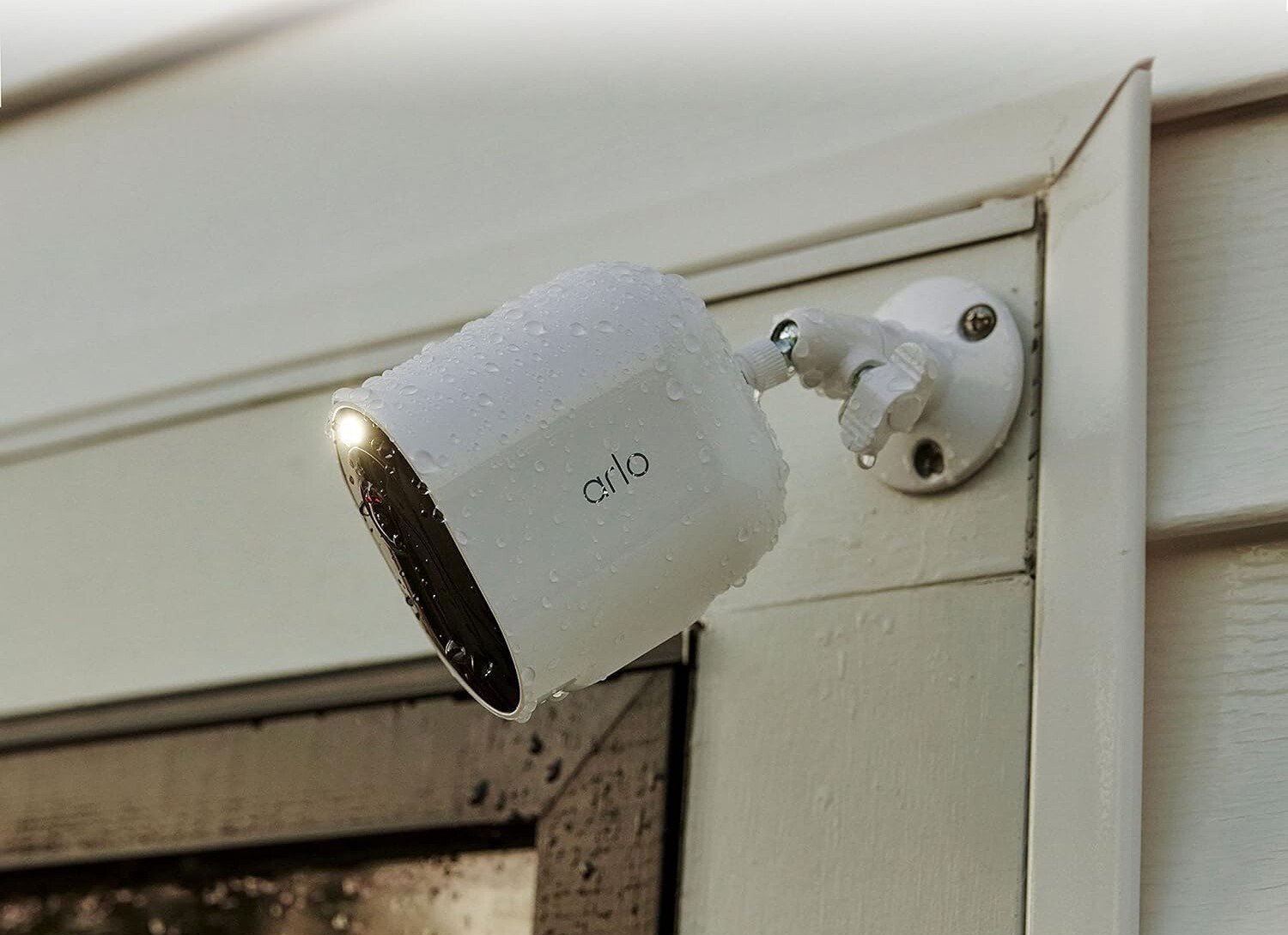 an arlo spotlight camera sits on the outside of a home, near the garage and is covered in rain drops