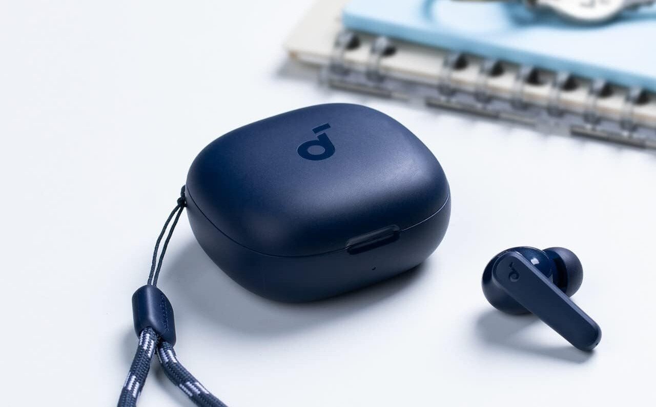 a navy blue pair of the anker p20i earbuds with included carrying case sitting on a white desk with a spiral notebook off in the right corner