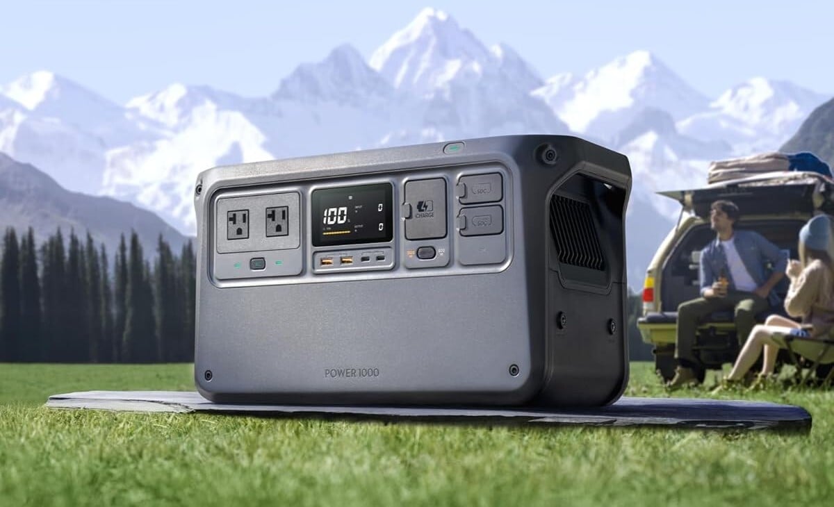 the dji power 1000 portable power station sits on the ground in green grass with snow-capped mountains in the background