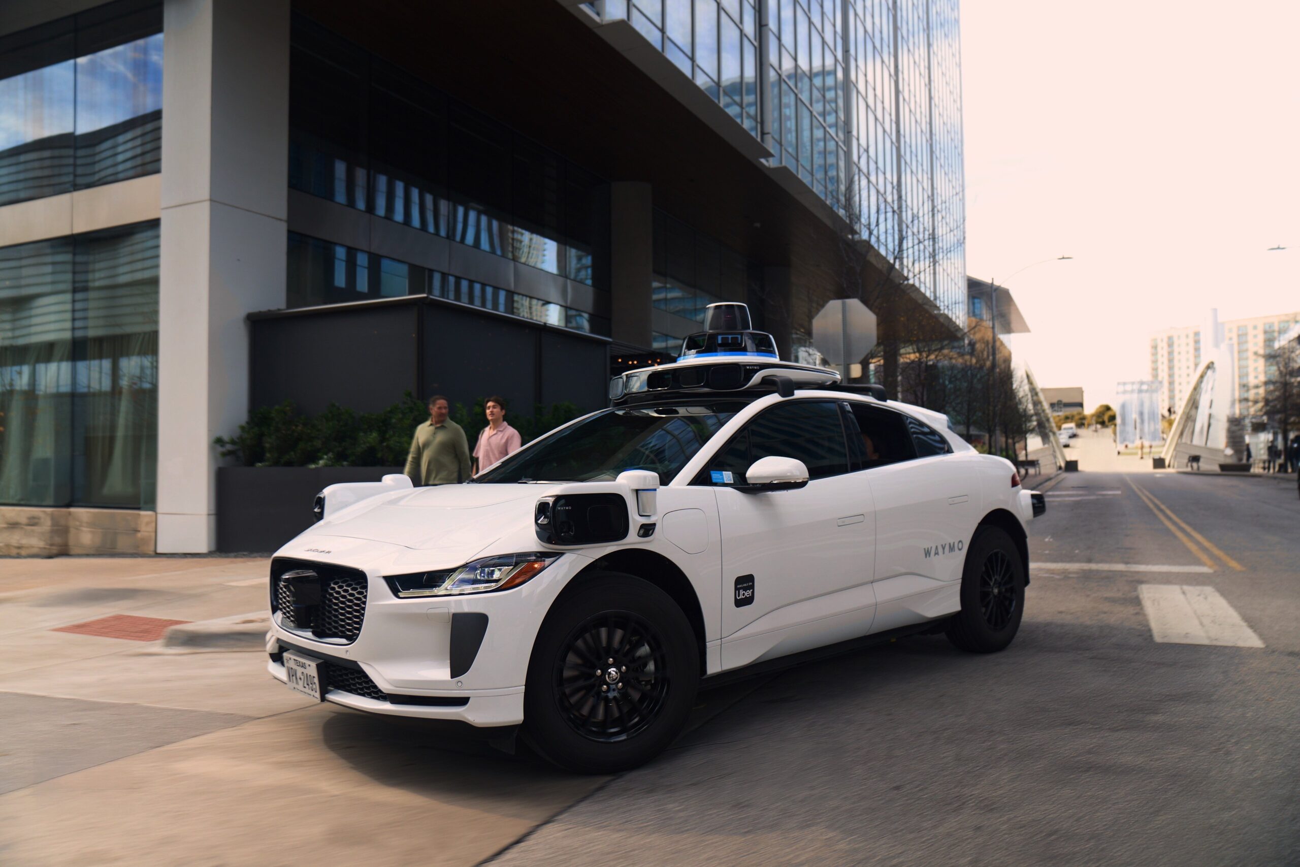 white Uber and Waymo co-branded autonomous SUV  parked at entrance of a building 