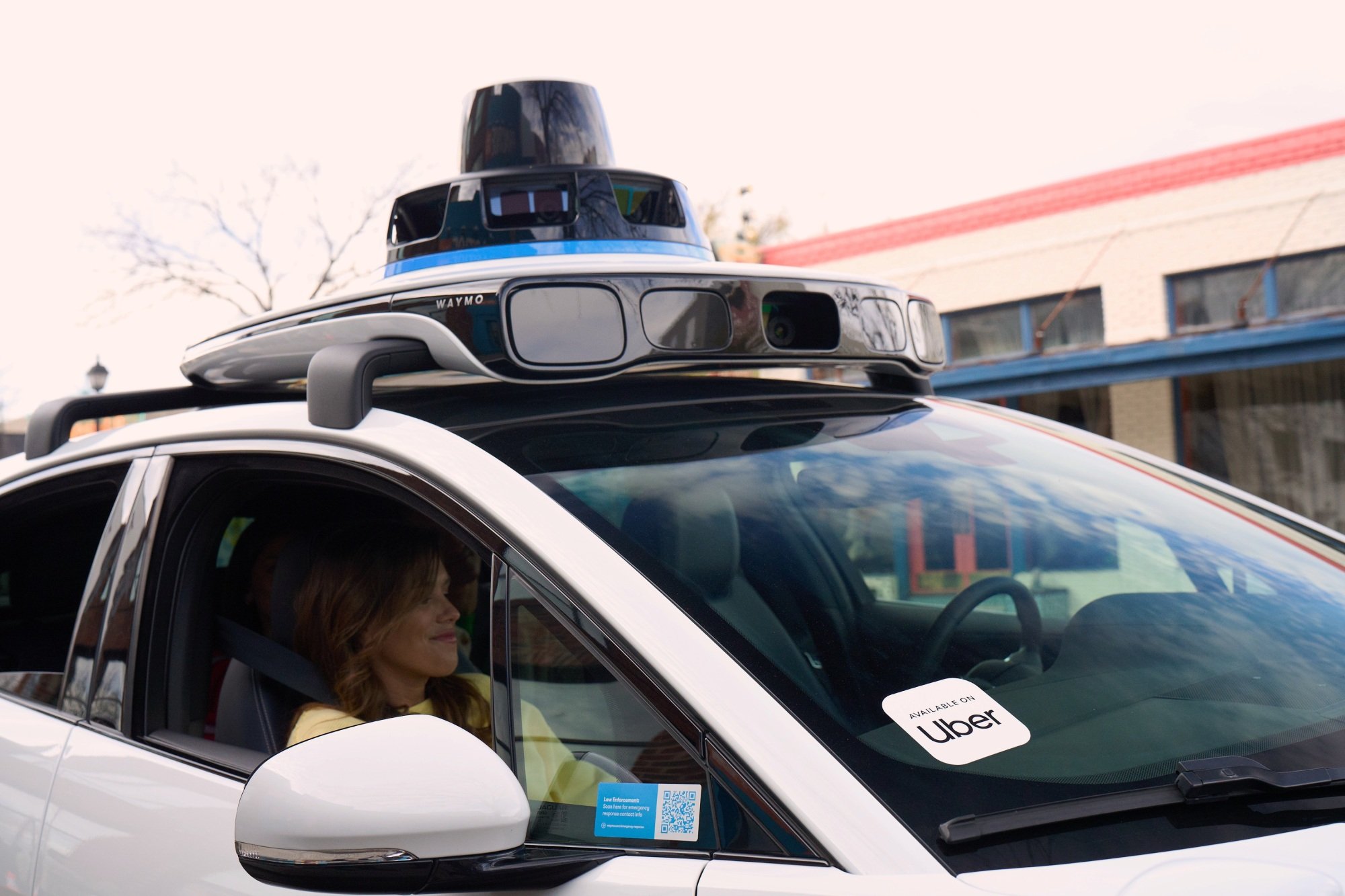 A close up of a woman in the passenger seat of a co-branded waymo and uber autonomous vehicle.