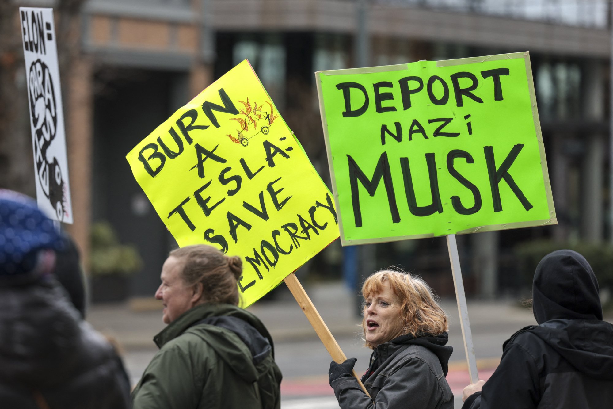 Two protesters hold signs that read "Burn a Tesla, save democracy" and "Deport Nazi Musk".
