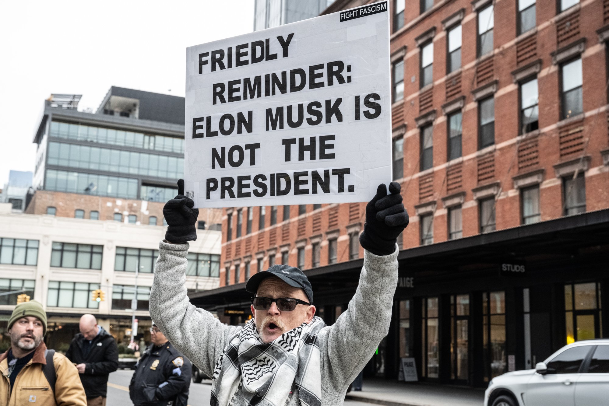 A protester holds a sign reading "Friendly reminder: Elon Musk is not the president."