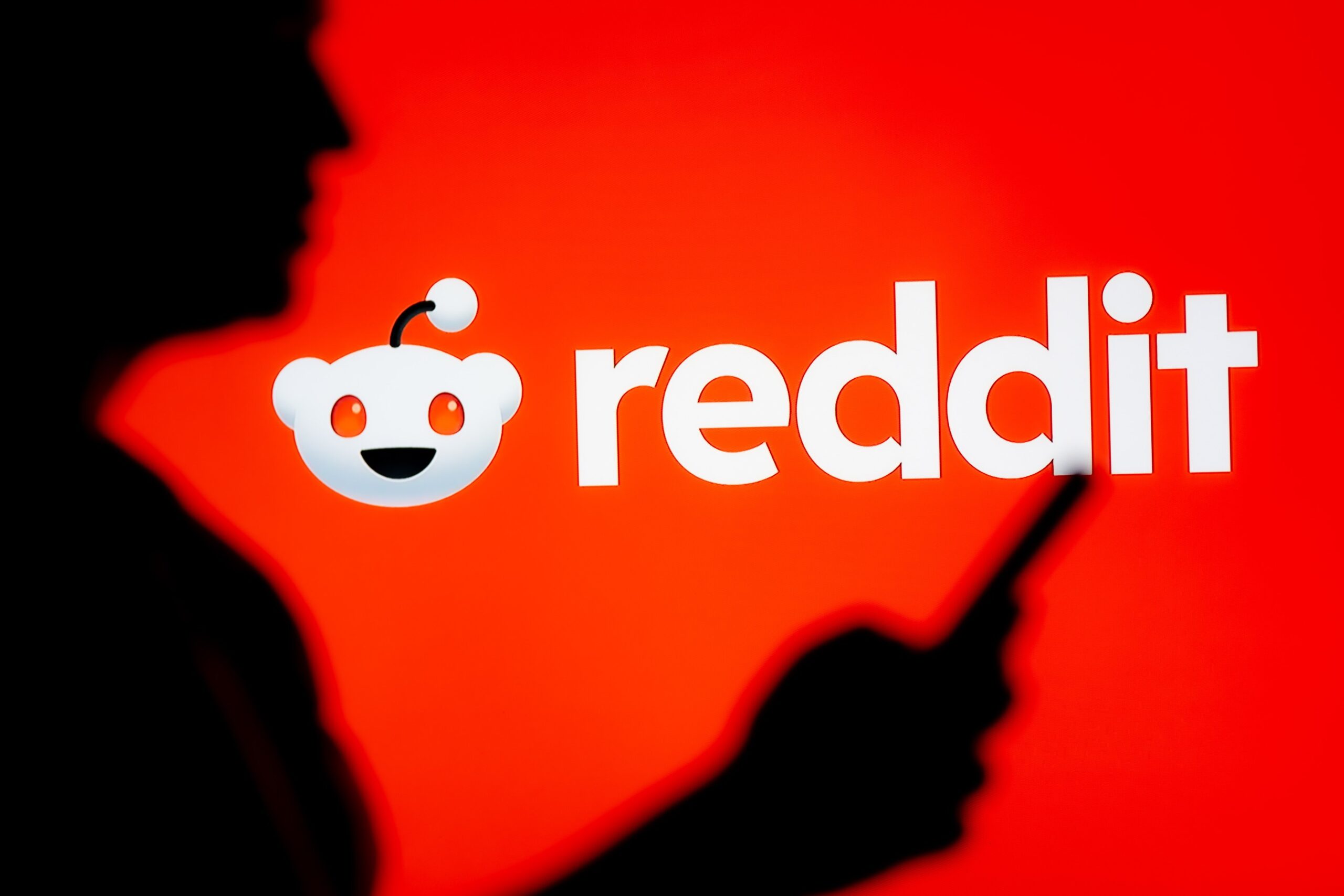 person looking at a smartphone with a Reddit logo displayed in the background