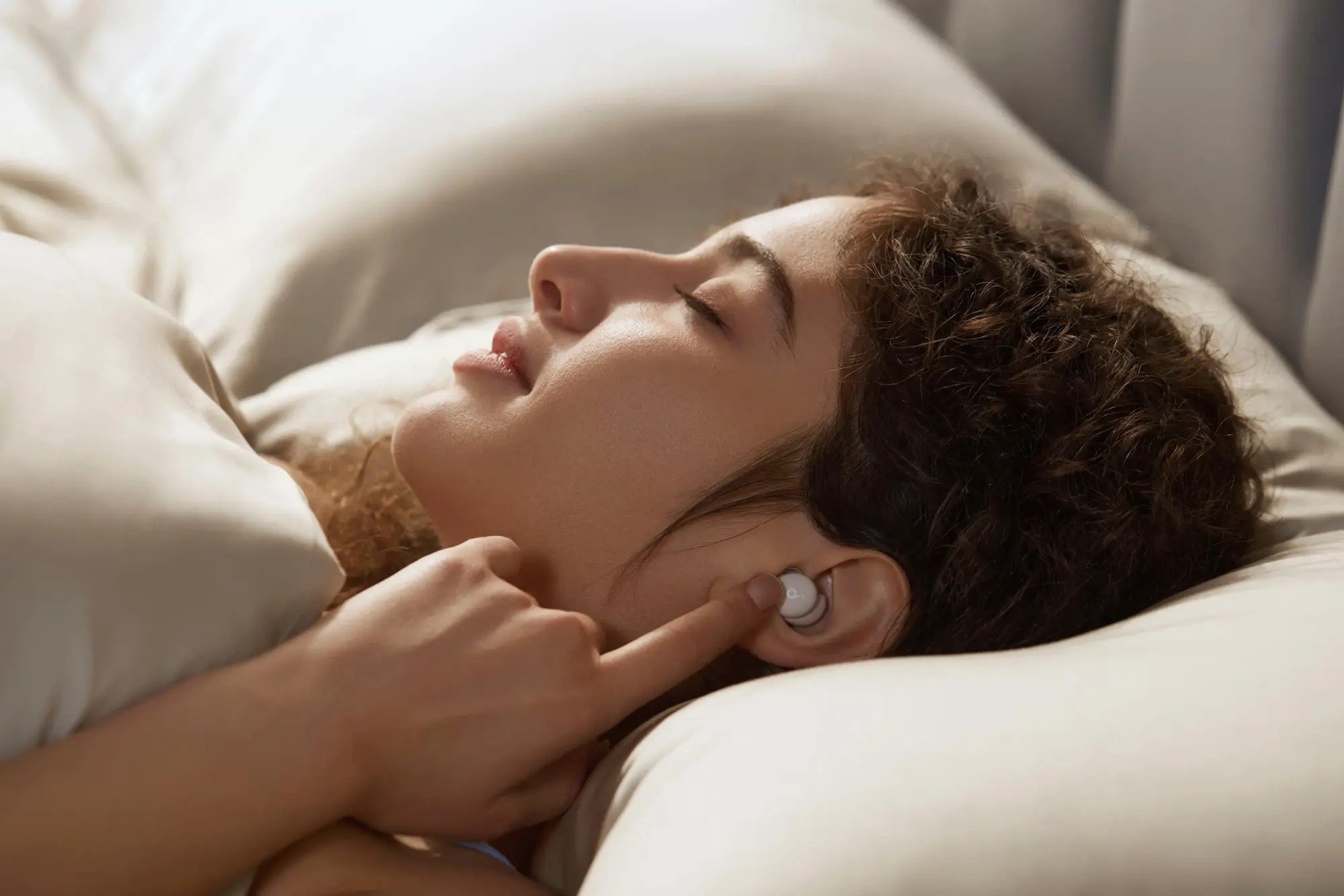 a person in bed touches an index finger to an anker sleep a20 earbud that's in her ear