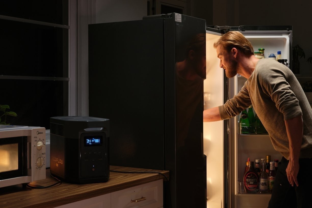 the EcoFlow Delta 2 Max portable power station sits on a kitchen countertop providing power for a refrigerator while a person is standing in front of the open fridge removing some food