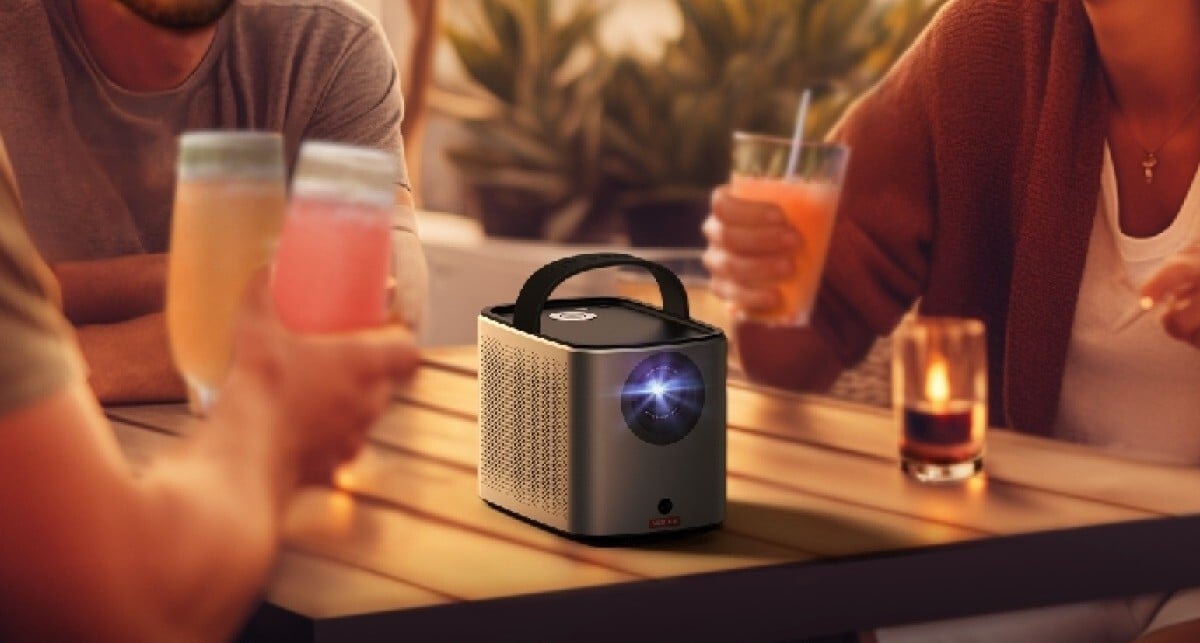 the nebula projector sits on a table outside with several drinks on it while people sit around the table