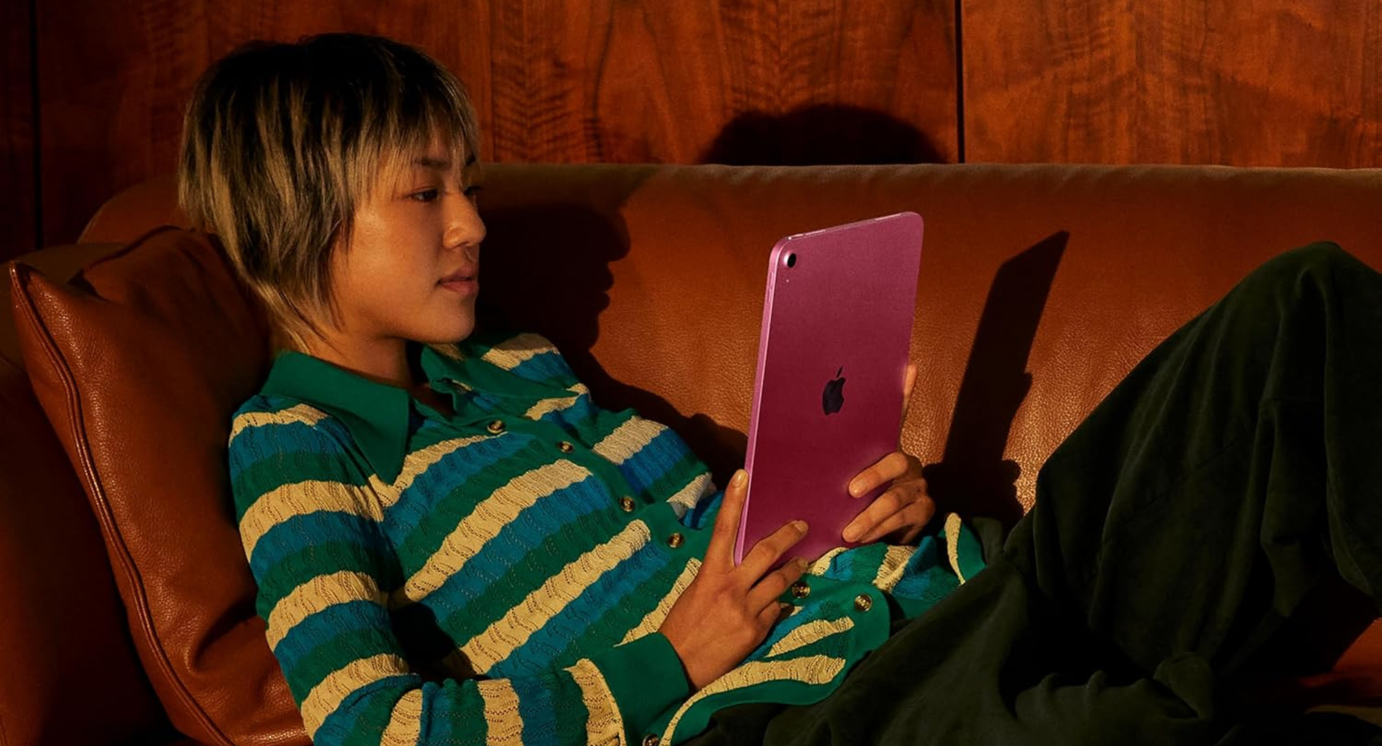 Person laying on a couch and holding a pink Apple ipad.