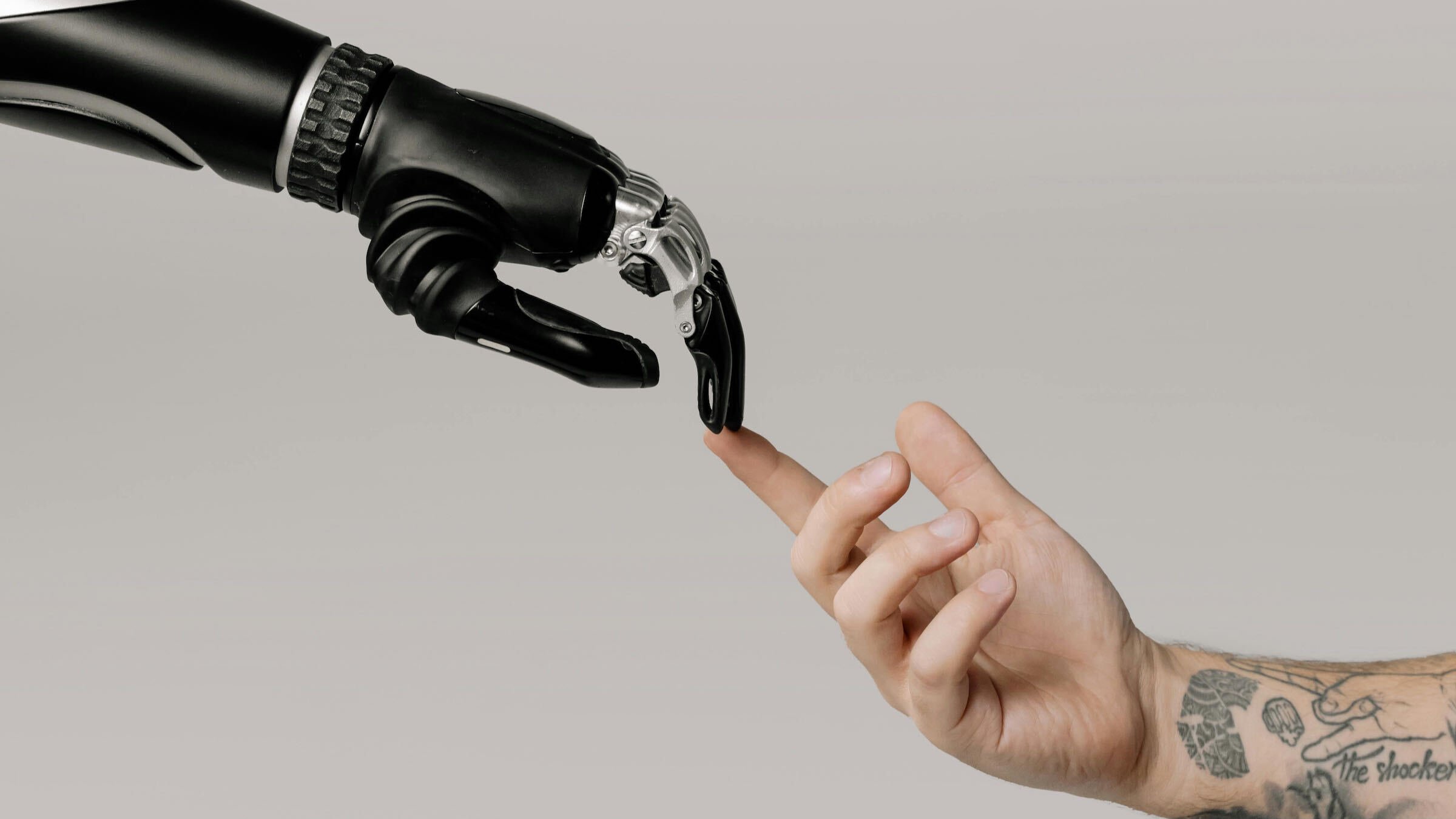 a black robot hand touching a tattooed arm