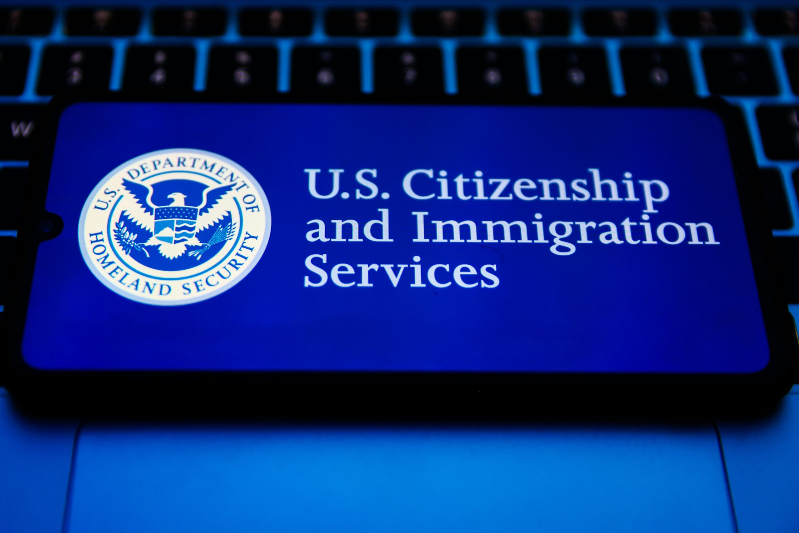 A cell phone displaying the US citizenship and immigration services logo rests on a keyboard.