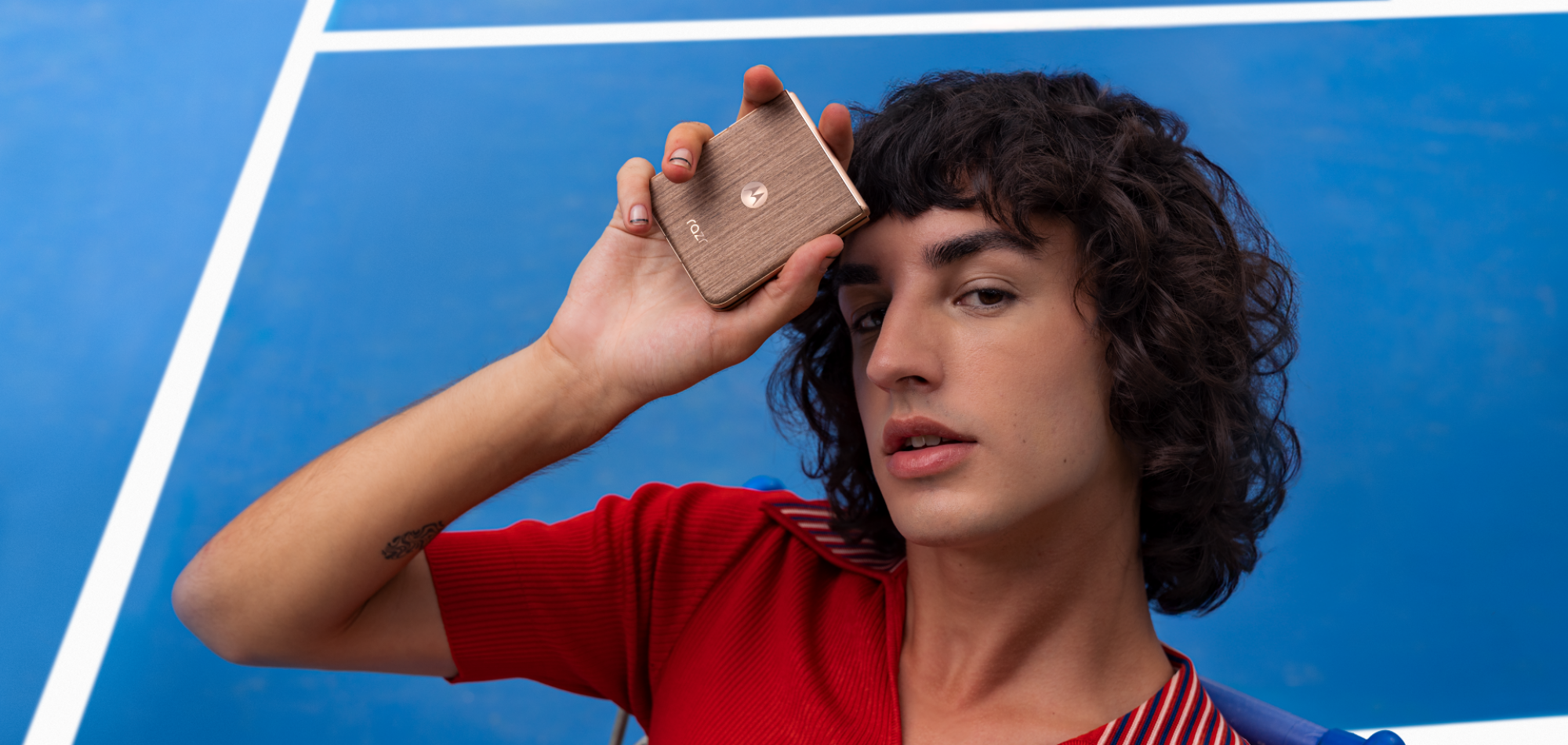 a hip man with curly hair holds the foldable motorola razr with a wood finish