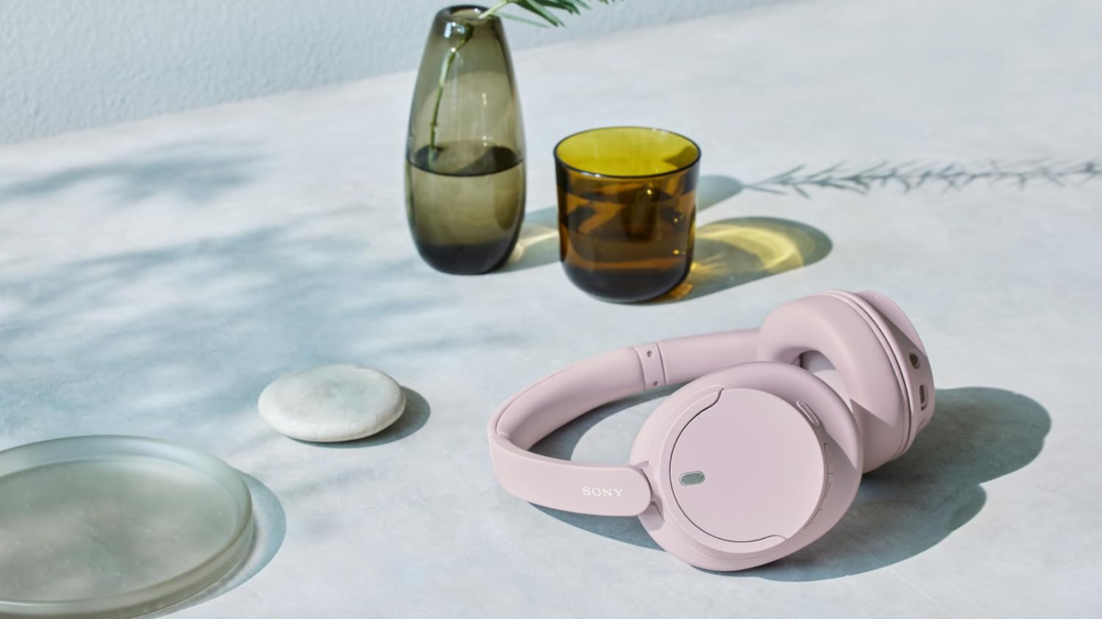 Sony WH-CH720 headphones in pink laying on table with cups