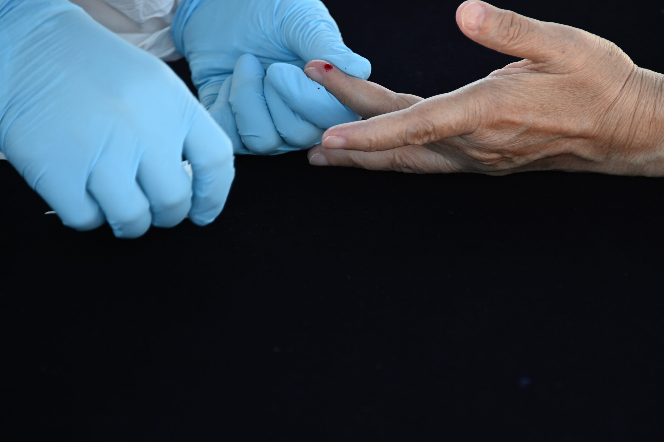 gloved hands pricking a finger for blood