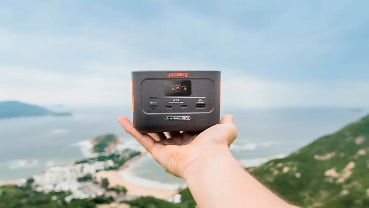 the jackery 100 plus portable power station sits in someone's hand while they stand on a mountain overlooking the ocean