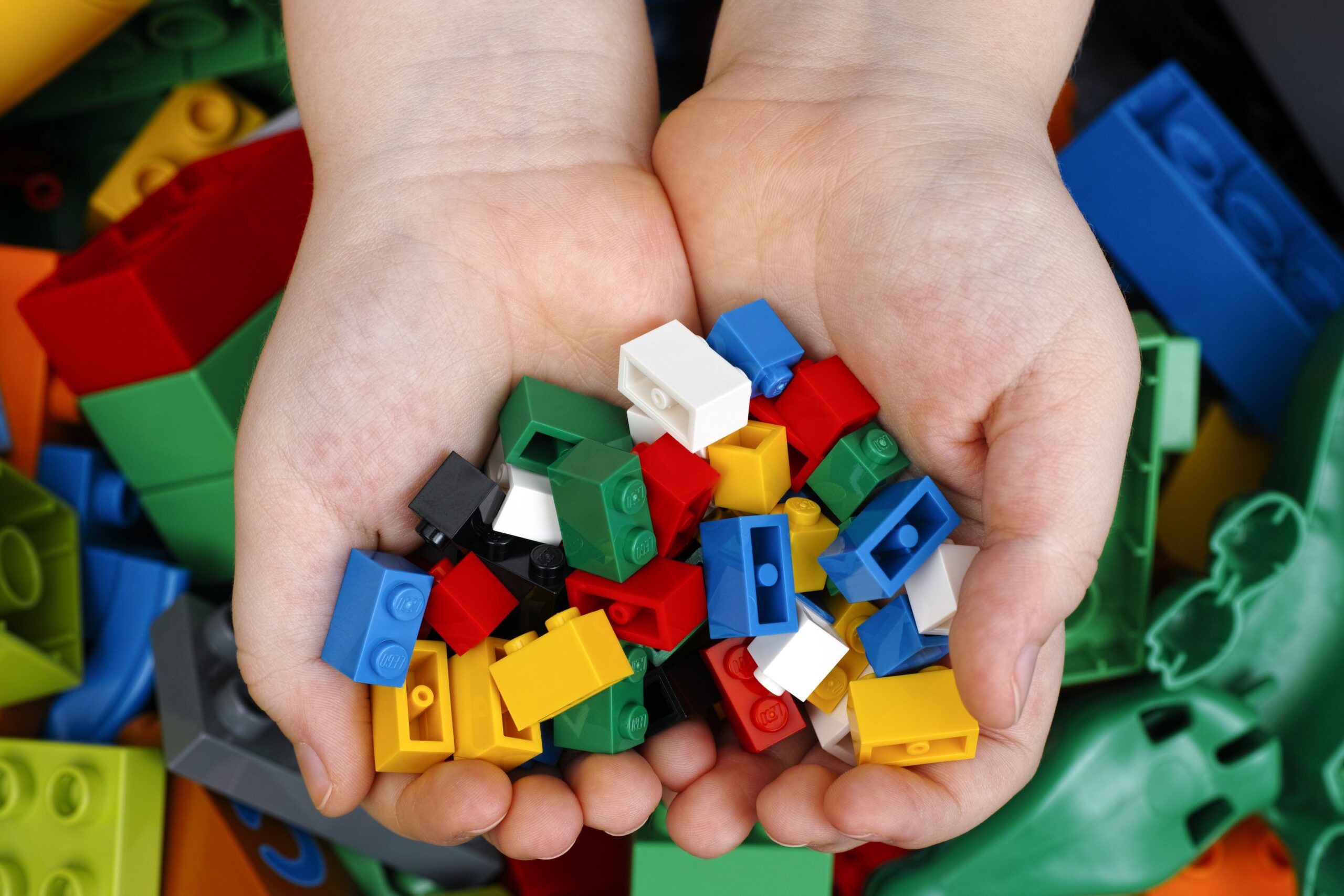 Lego Bricks in child's hands with Lego Duplo blocks and toys background