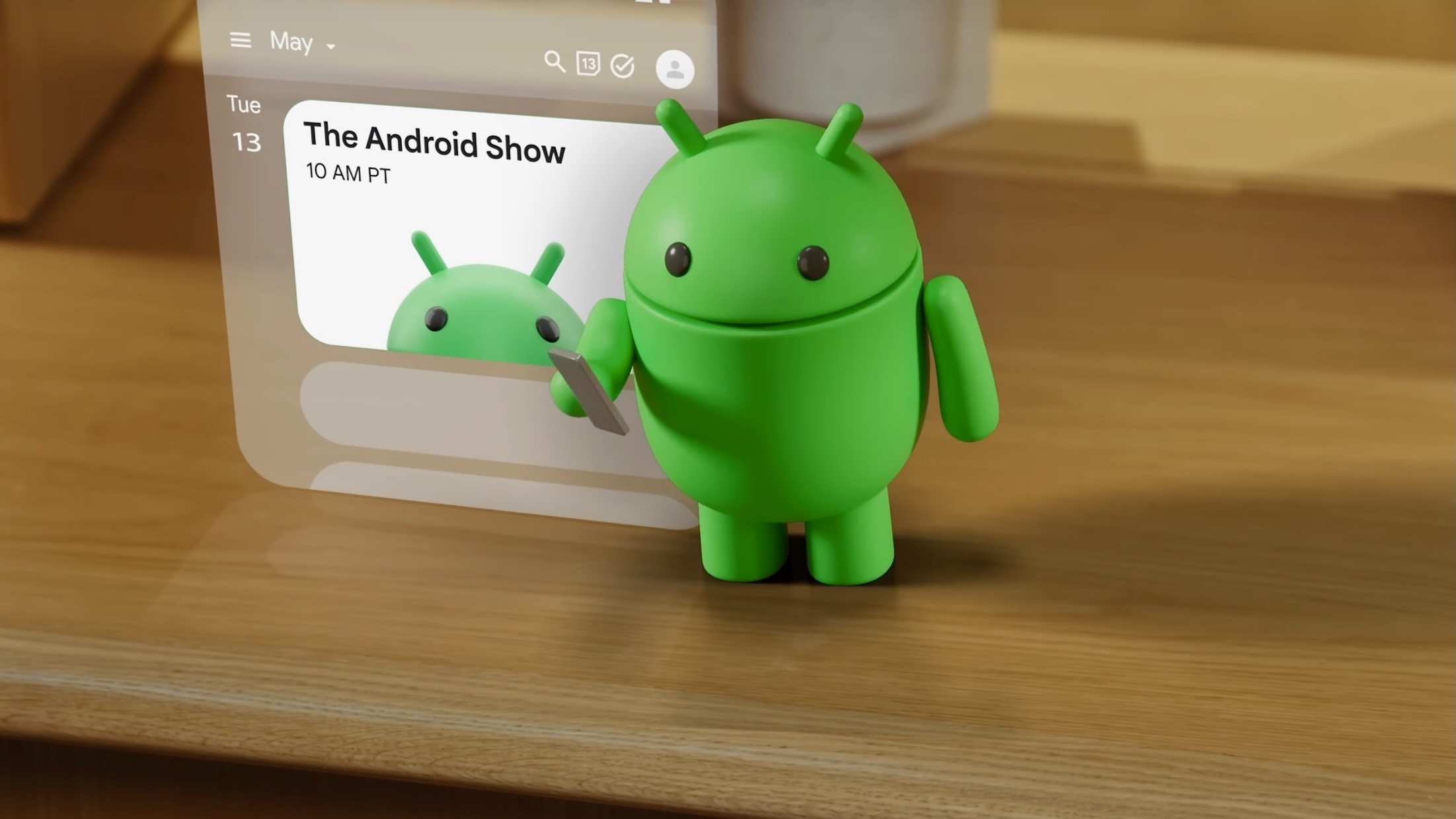 A 3D Android mascot holding a phone stands next to a floating digital calendar showing 'The Android Show'