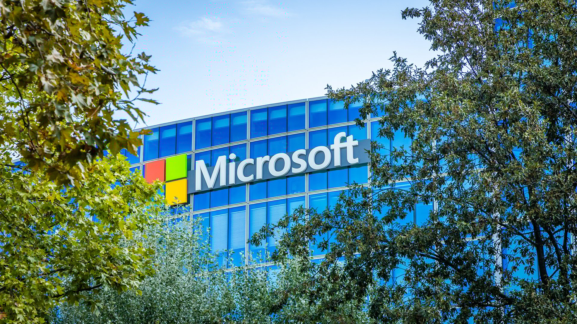 A Microsoft logo is seen on an office building through the trees.