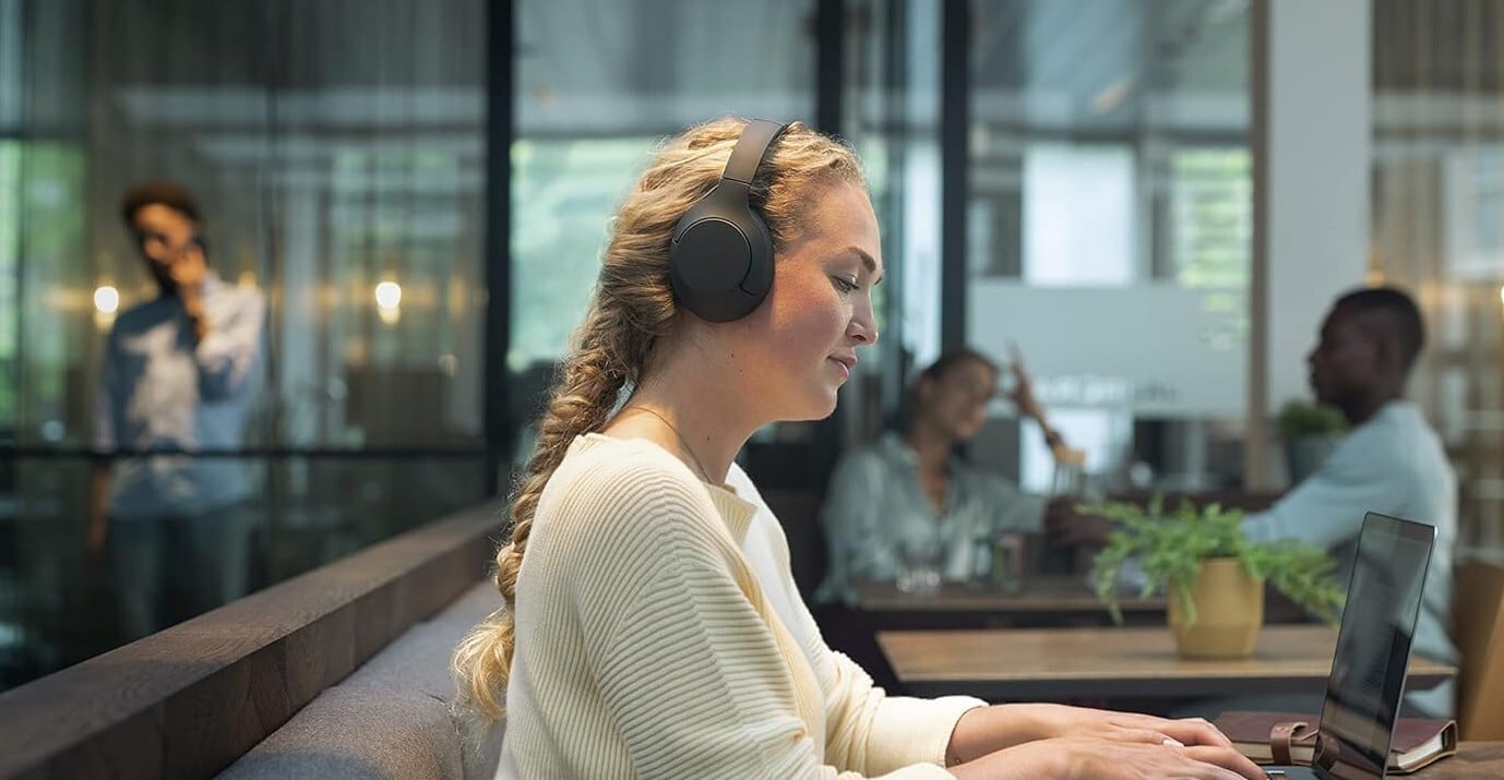 a person wears the philips headphones while working on a laptop and smiling slightly