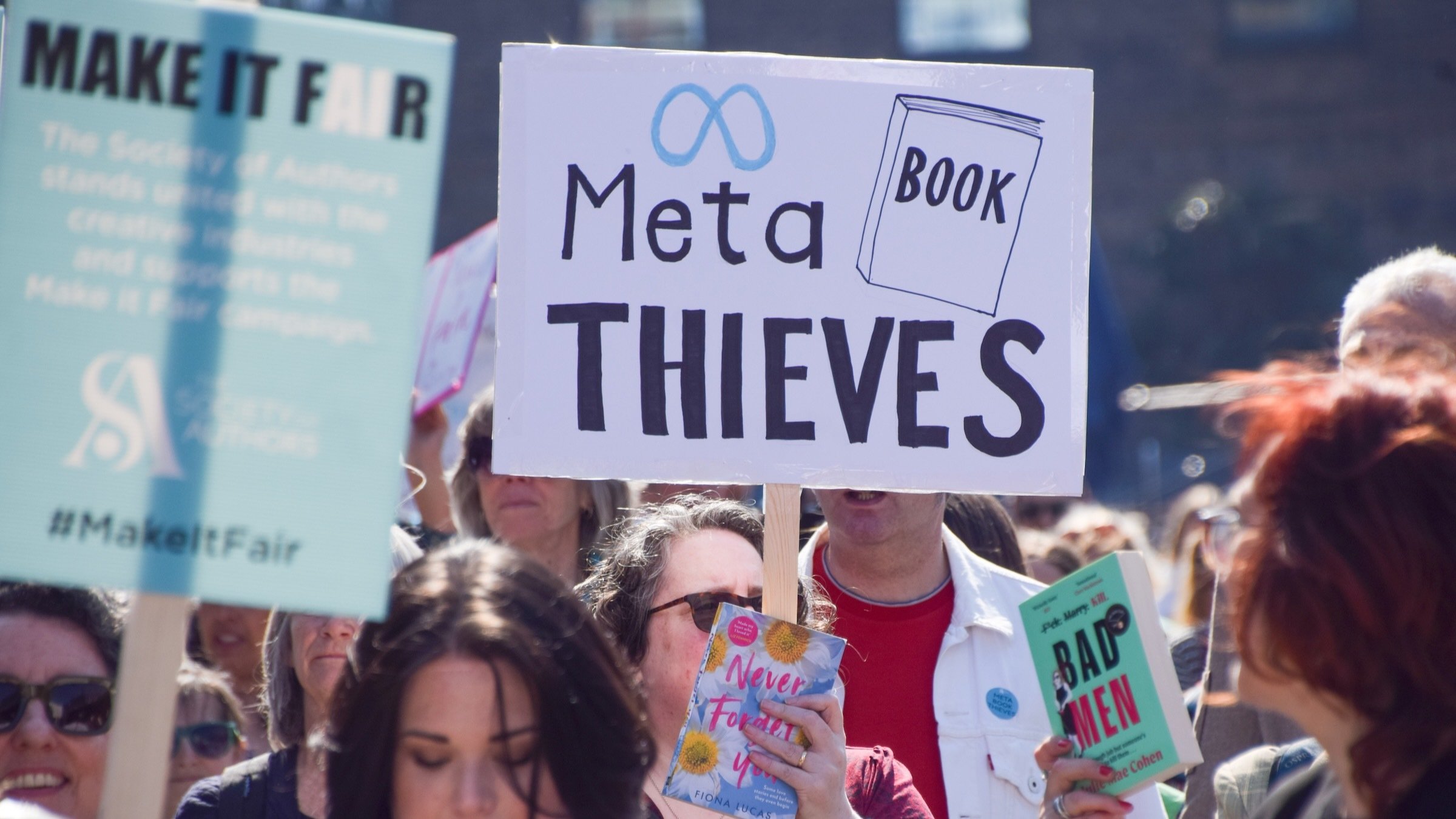A protester holds a 'Meta book thieves' placard in King's Cross during the march to Meta offices