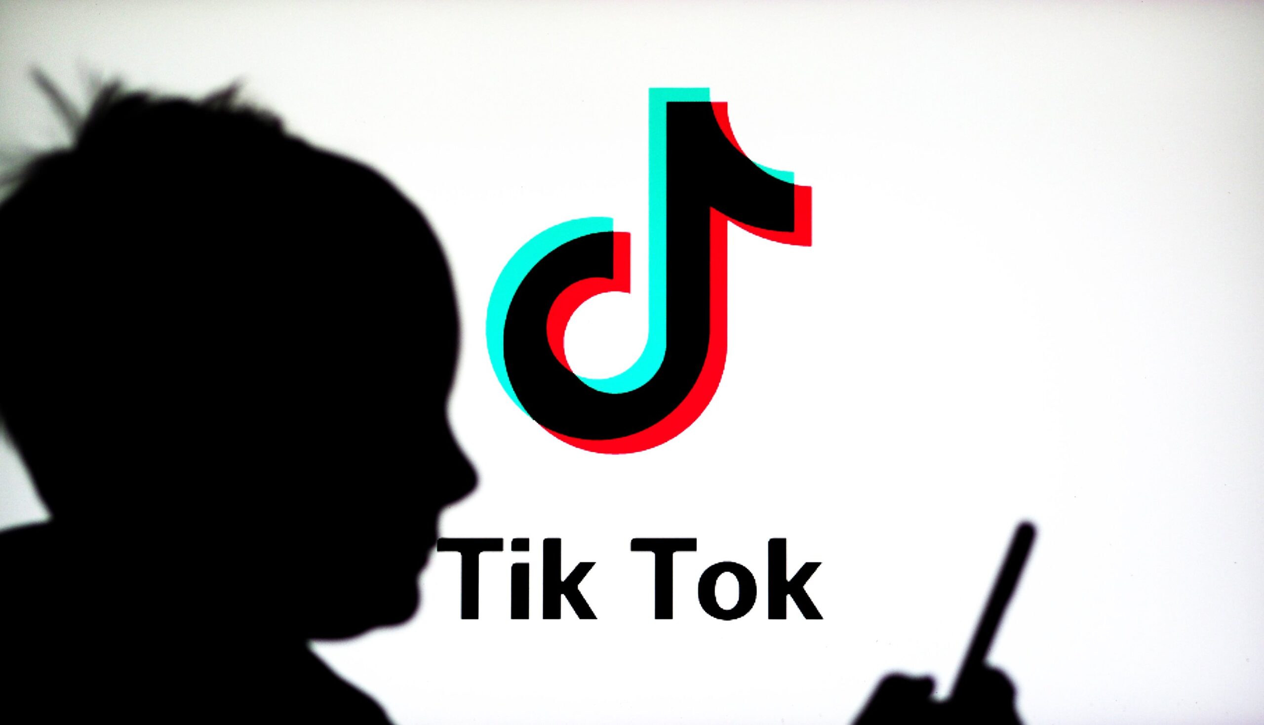 A TikTok logo seen on display with a child watching something on his phone.