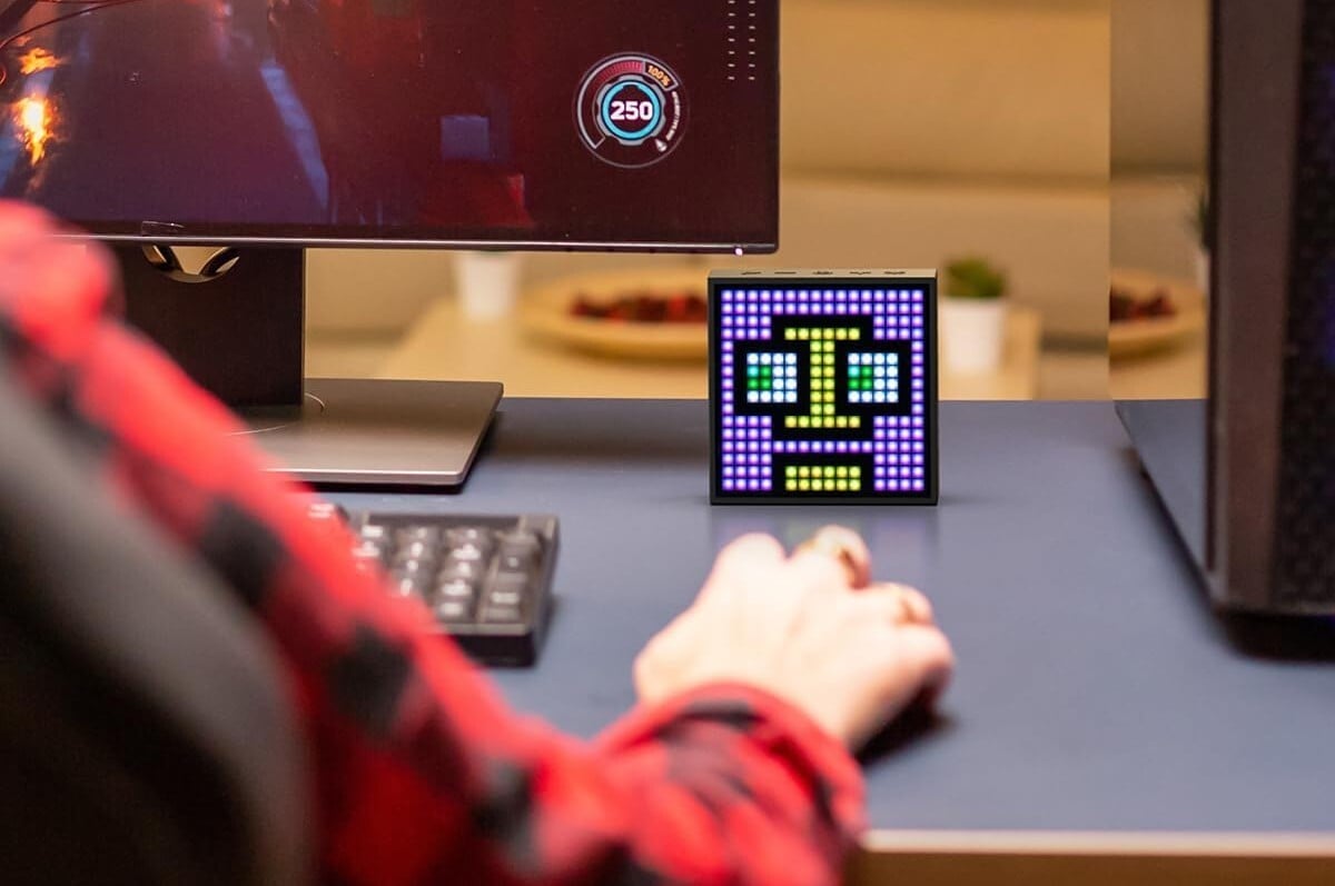 a divoom timebox evo sits on a desktop near a right hand that's controlling a mouse